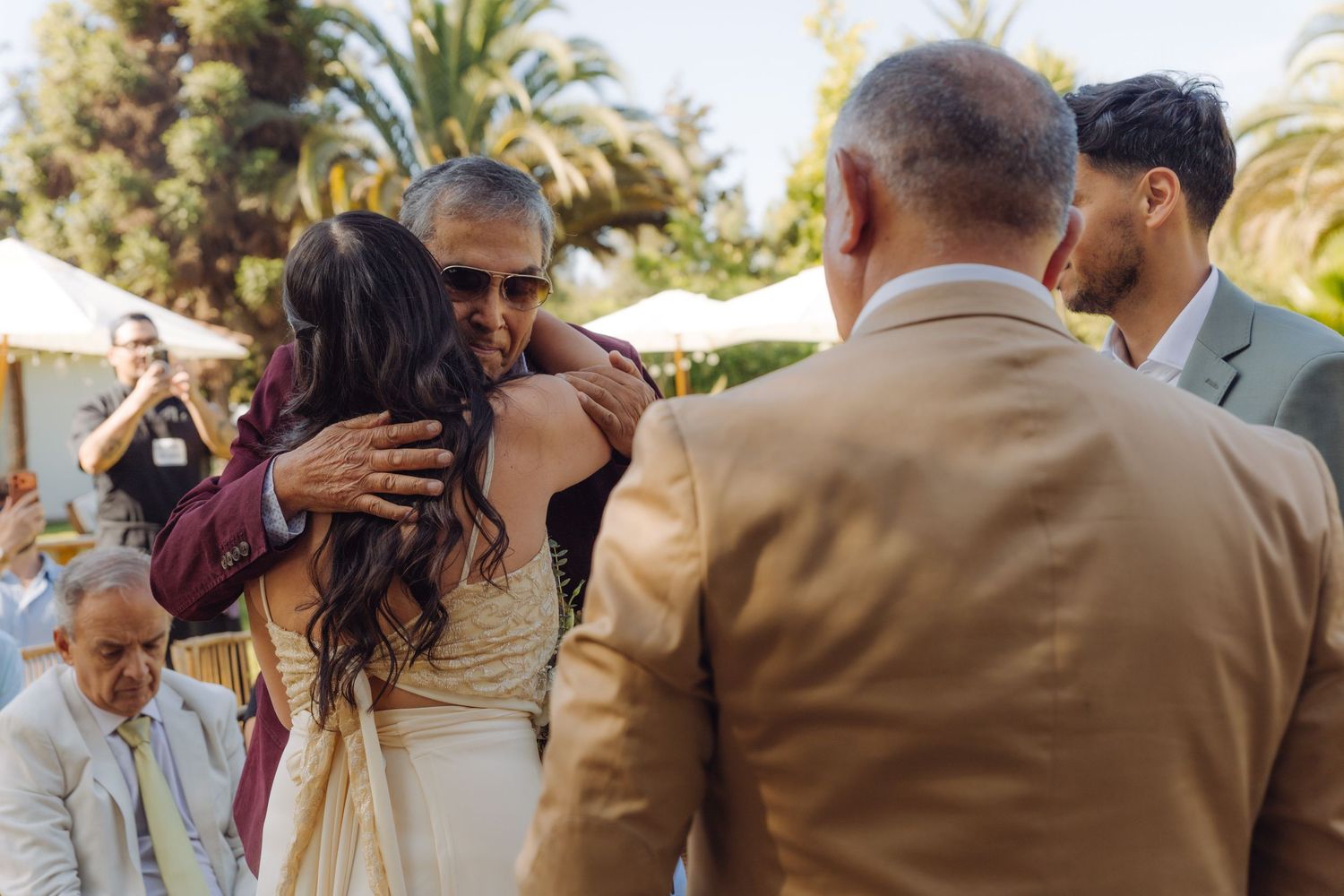 Emotional wedding moment as bride receives warm hug from family member during outdoor ceremony.