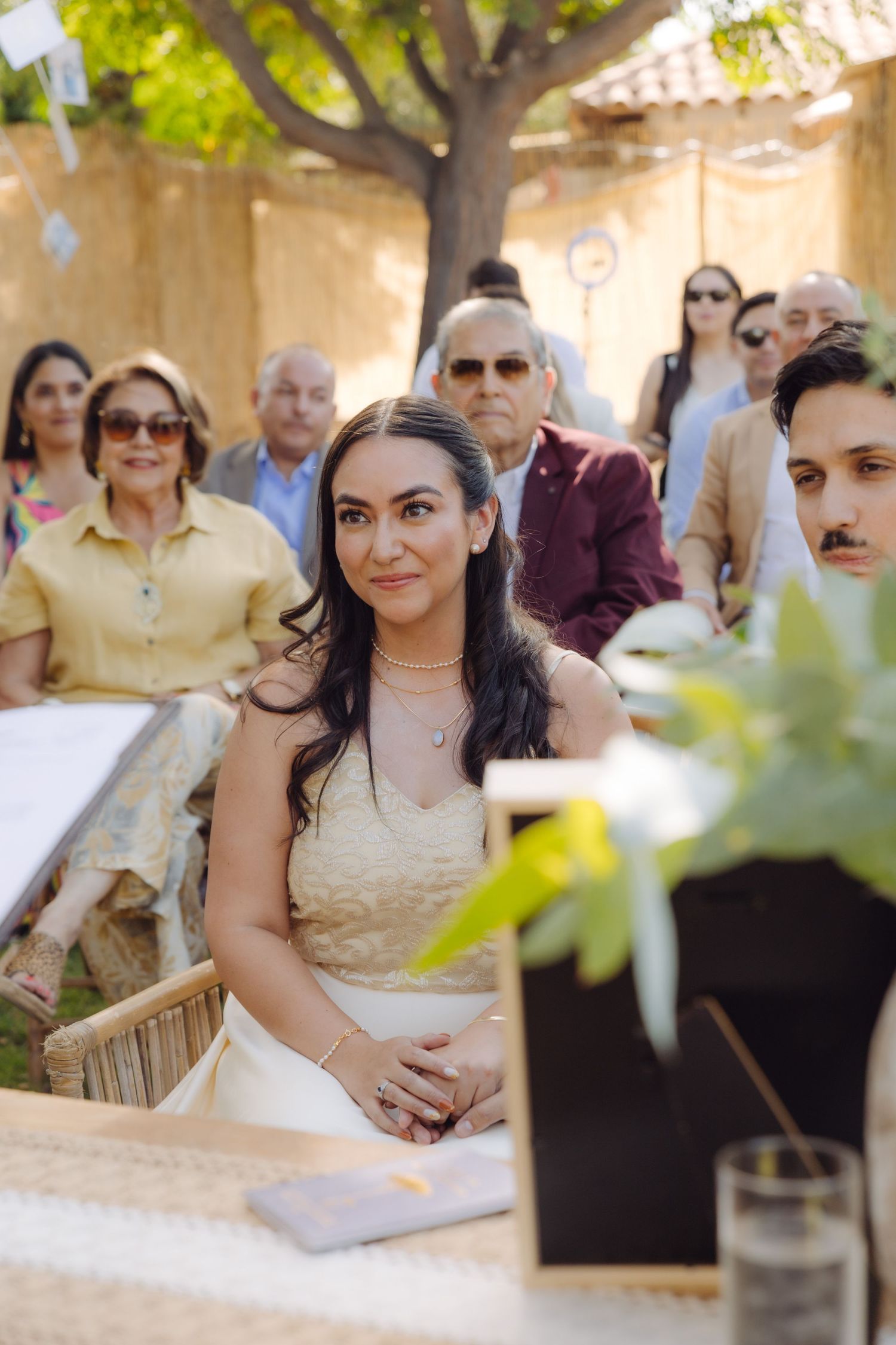 Beautiful bride smiles during outdoor garden wedding ceremony with guests seated behind her.