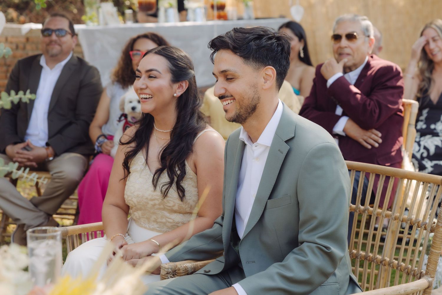 Smiling bride and groom share a joyful moment seated together during outdoor wedding ceremony.