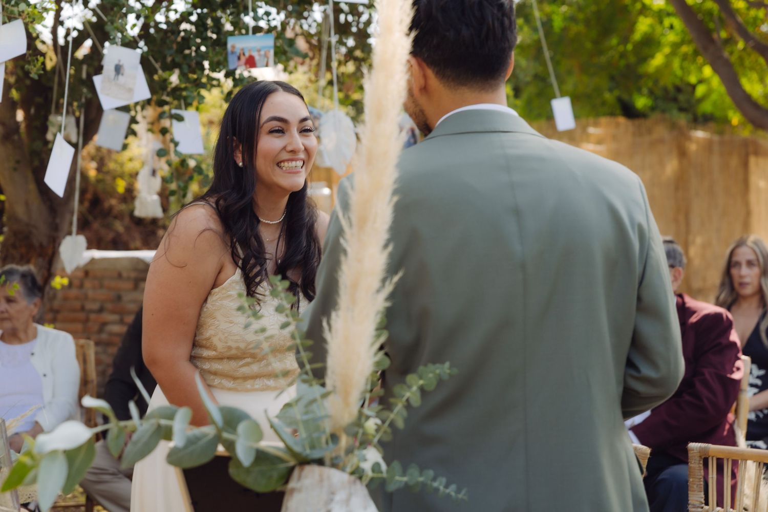 Radiant bride smiles at groom during intimate outdoor wedding ceremony with pampas grass decor.