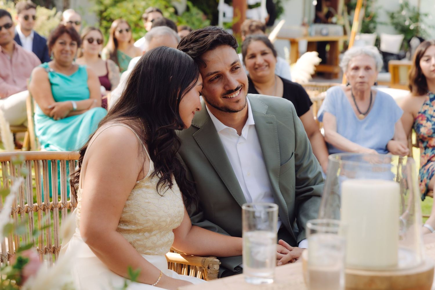 Smiling newlyweds share a joyful moment at their wedding reception table surrounded by family and floral centerpieces.