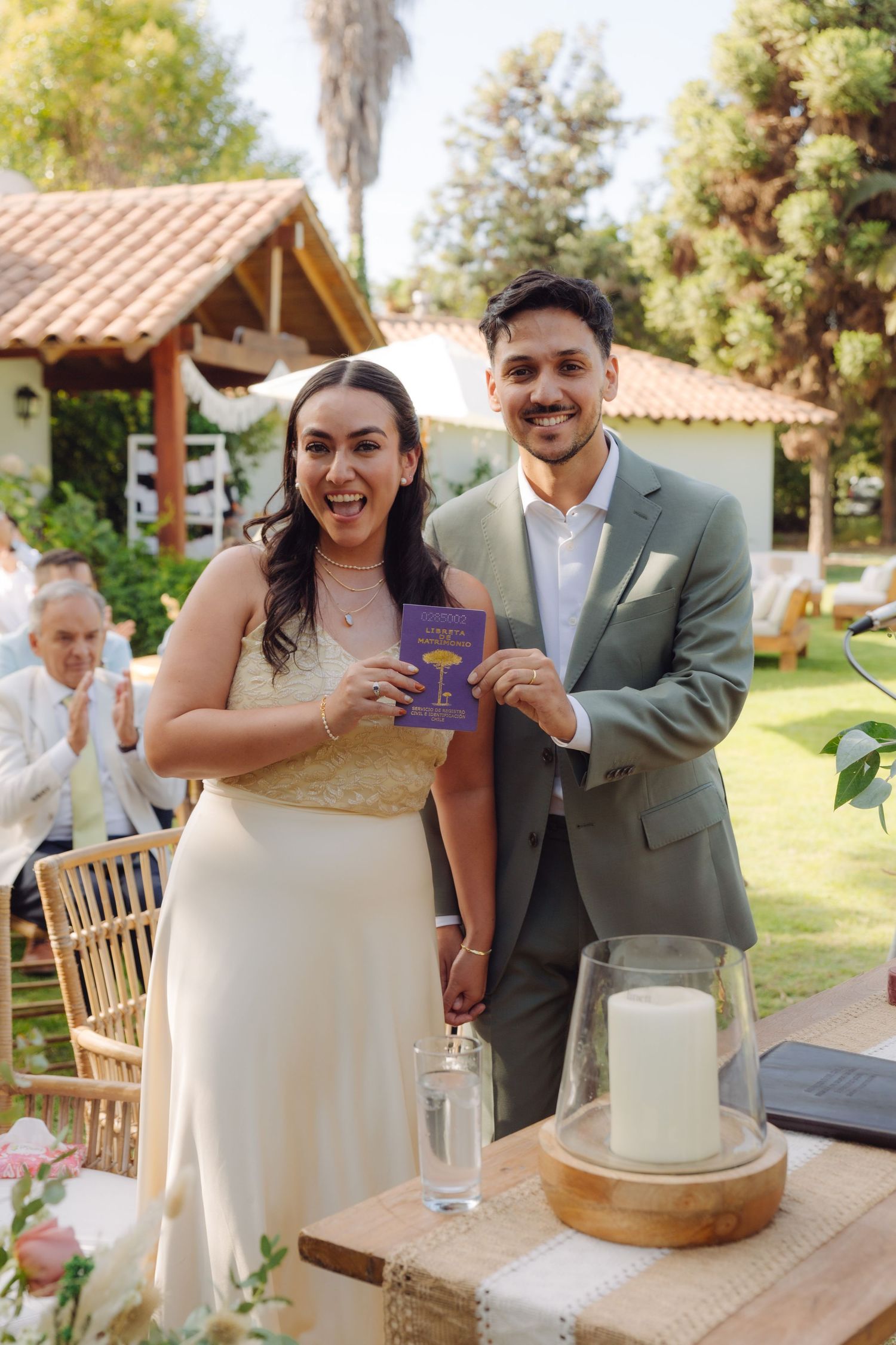 Happy bride and groom hold up their marriage certificate at an outdoor garden wedding ceremony.