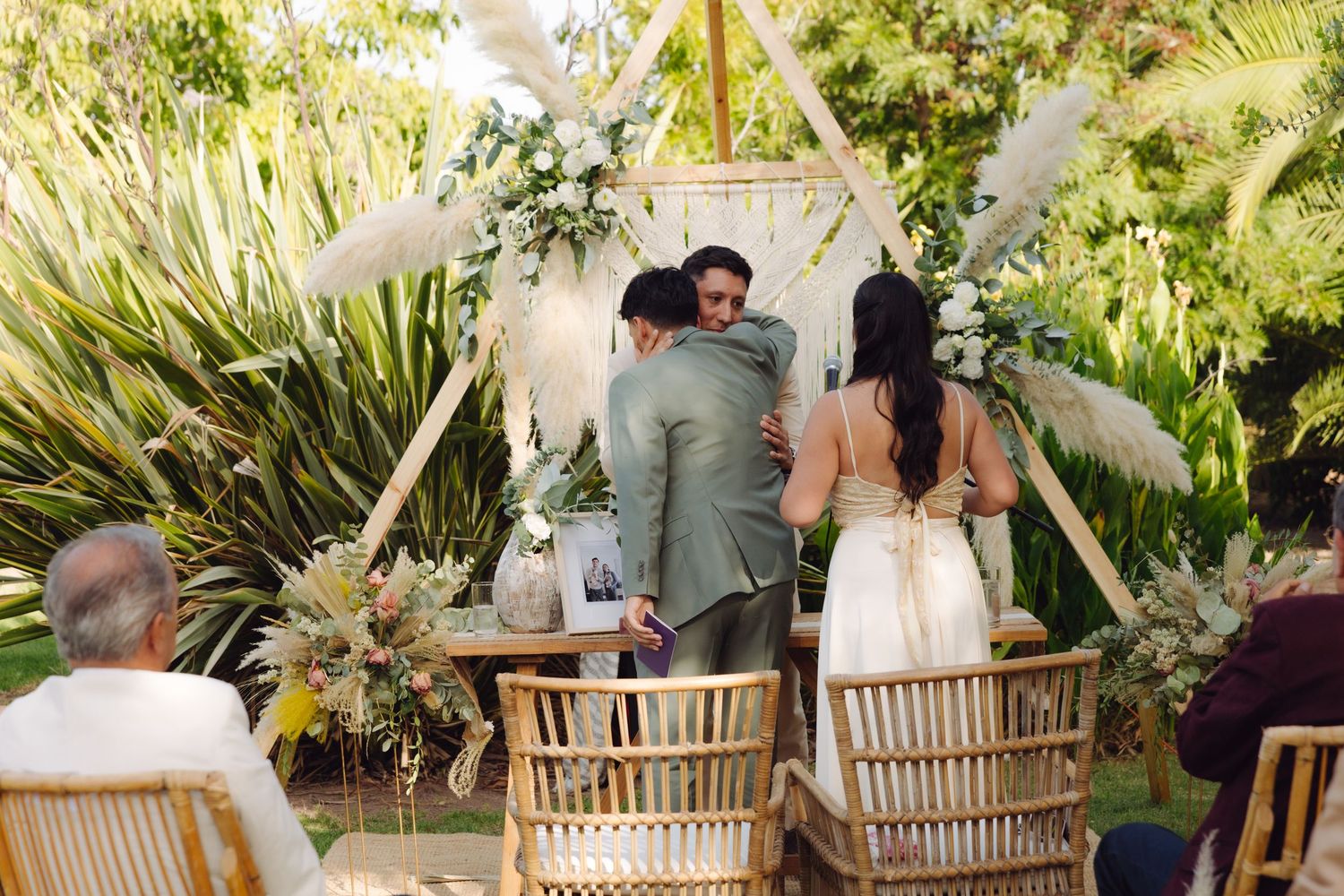 Wedding guests watch as couple embraces officiant at a boho outdoor ceremony altar.