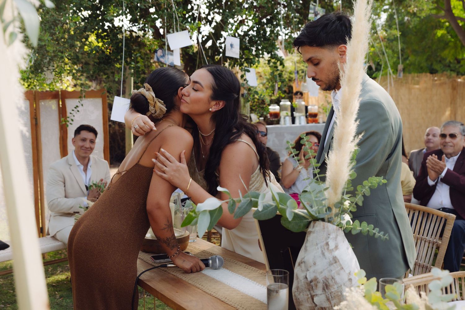 Woman in brown dress kisses bride on cheek at outdoor boho wedding ceremony.