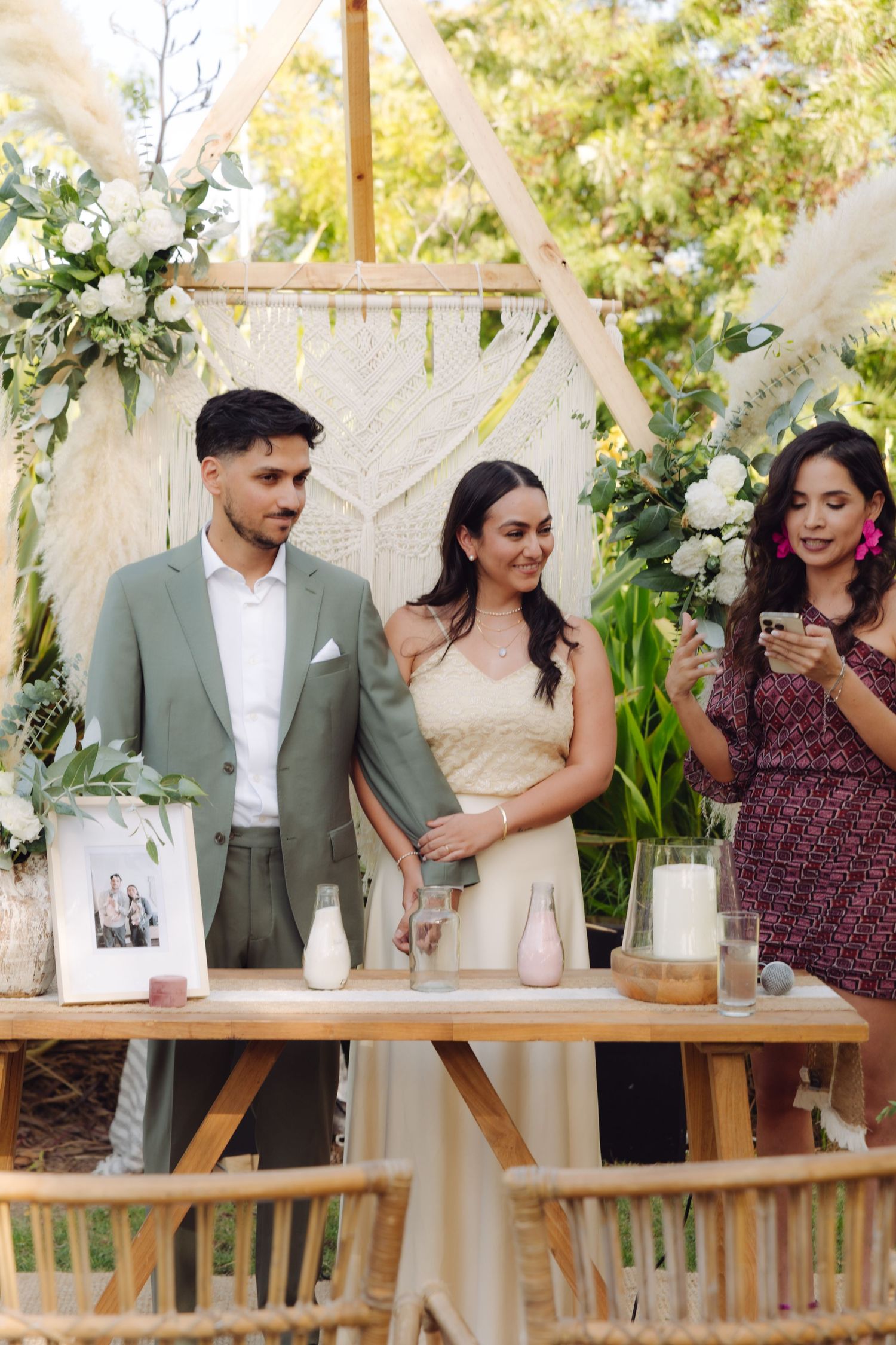 Bride and groom standing at altar with officiant during boho outdoor wedding ceremony.