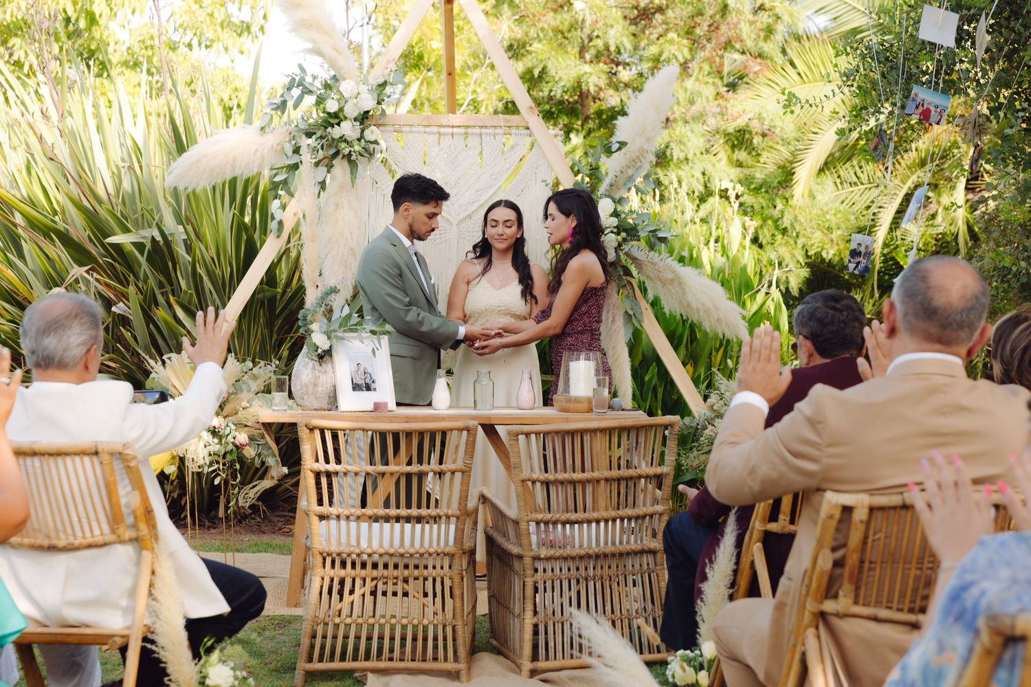 Couple exchanging vows at a boho outdoor wedding with guests seated in bamboo chairs.