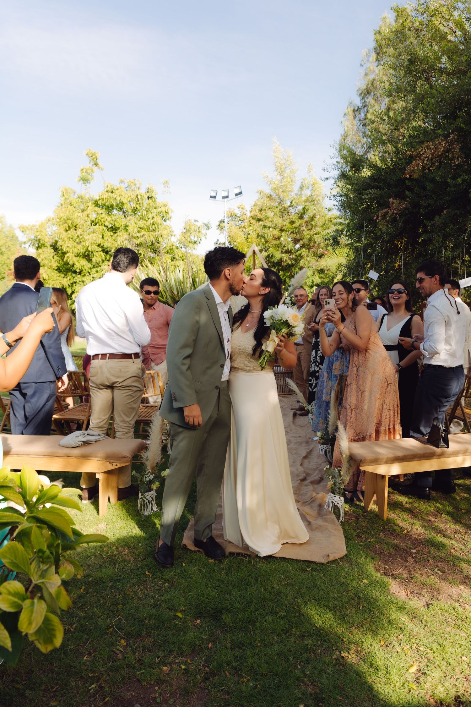 Newlyweds sharing a romantic kiss at the end of the aisle after outdoor wedding ceremony.