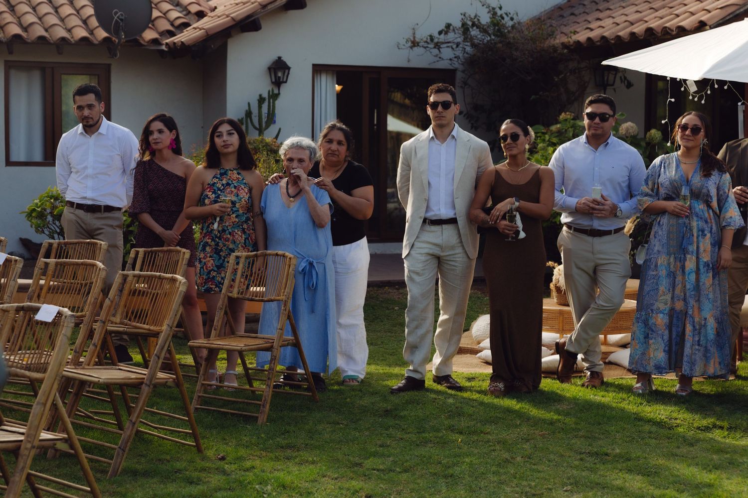 Wedding guests in formal attire standing on green lawn outside rustic venue during outdoor celebration.