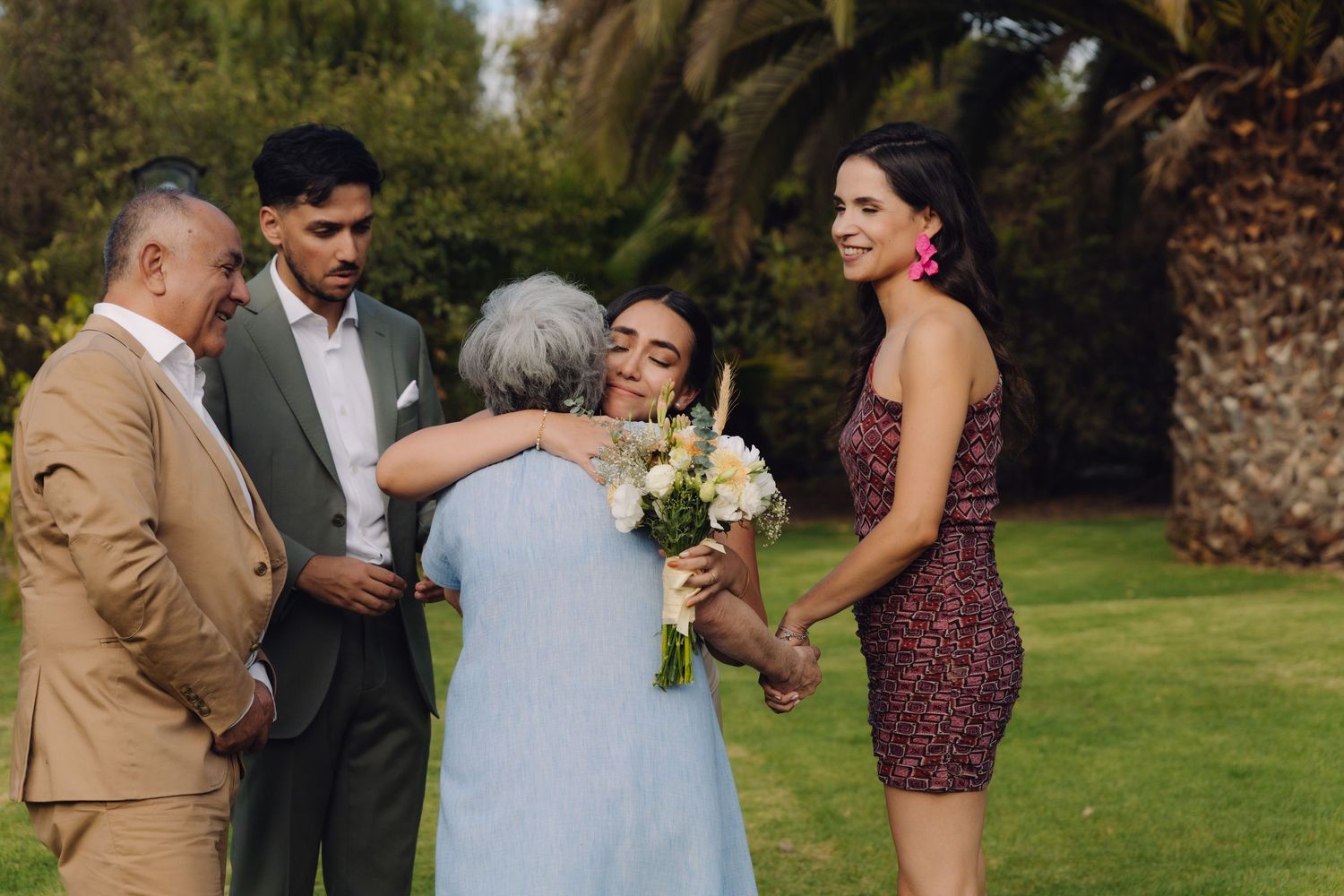 Bride embracing elderly guest while family members smile during outdoor wedding reception.