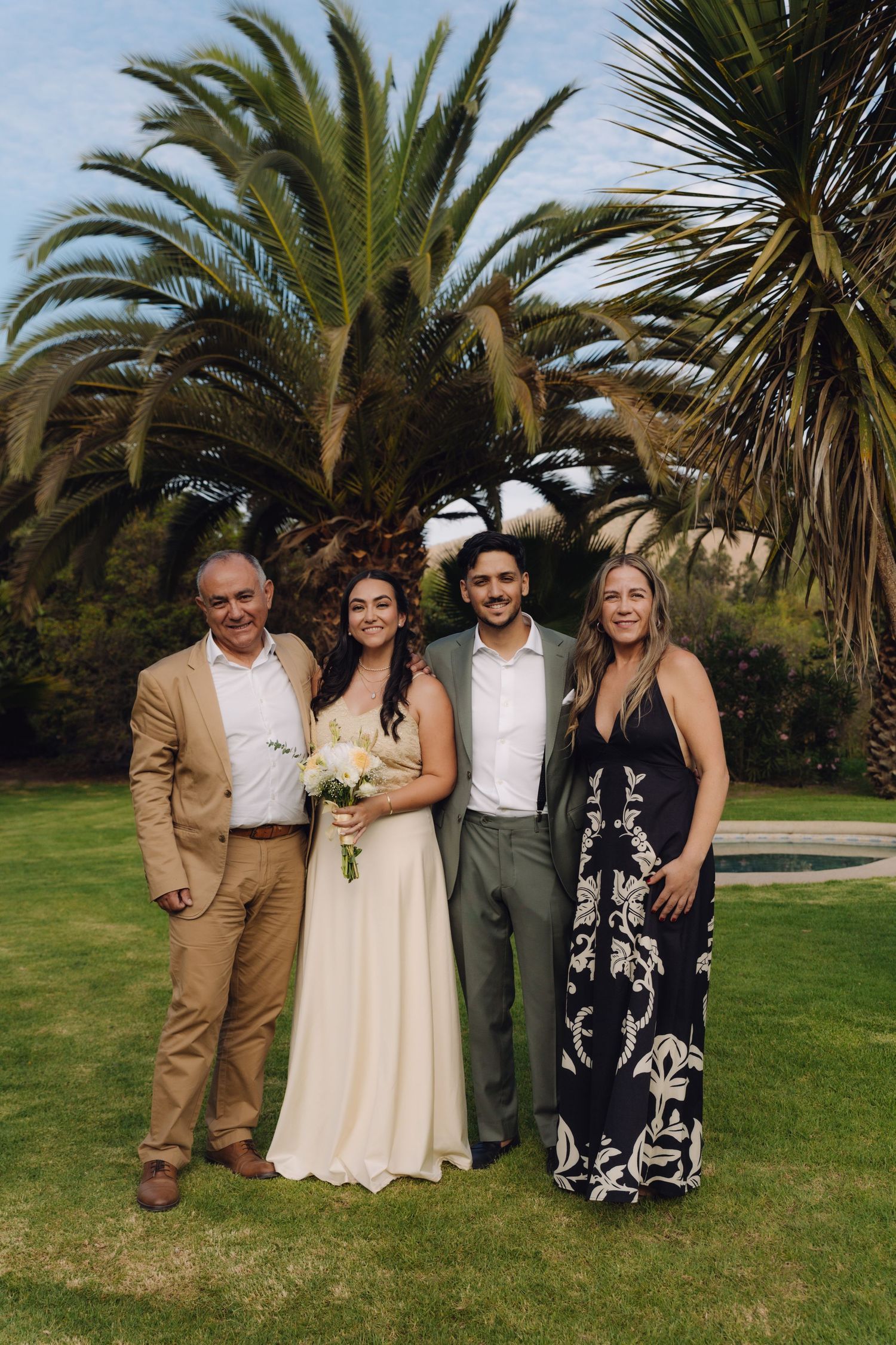 Bride and groom pose with two family members in front of tall palm tree.