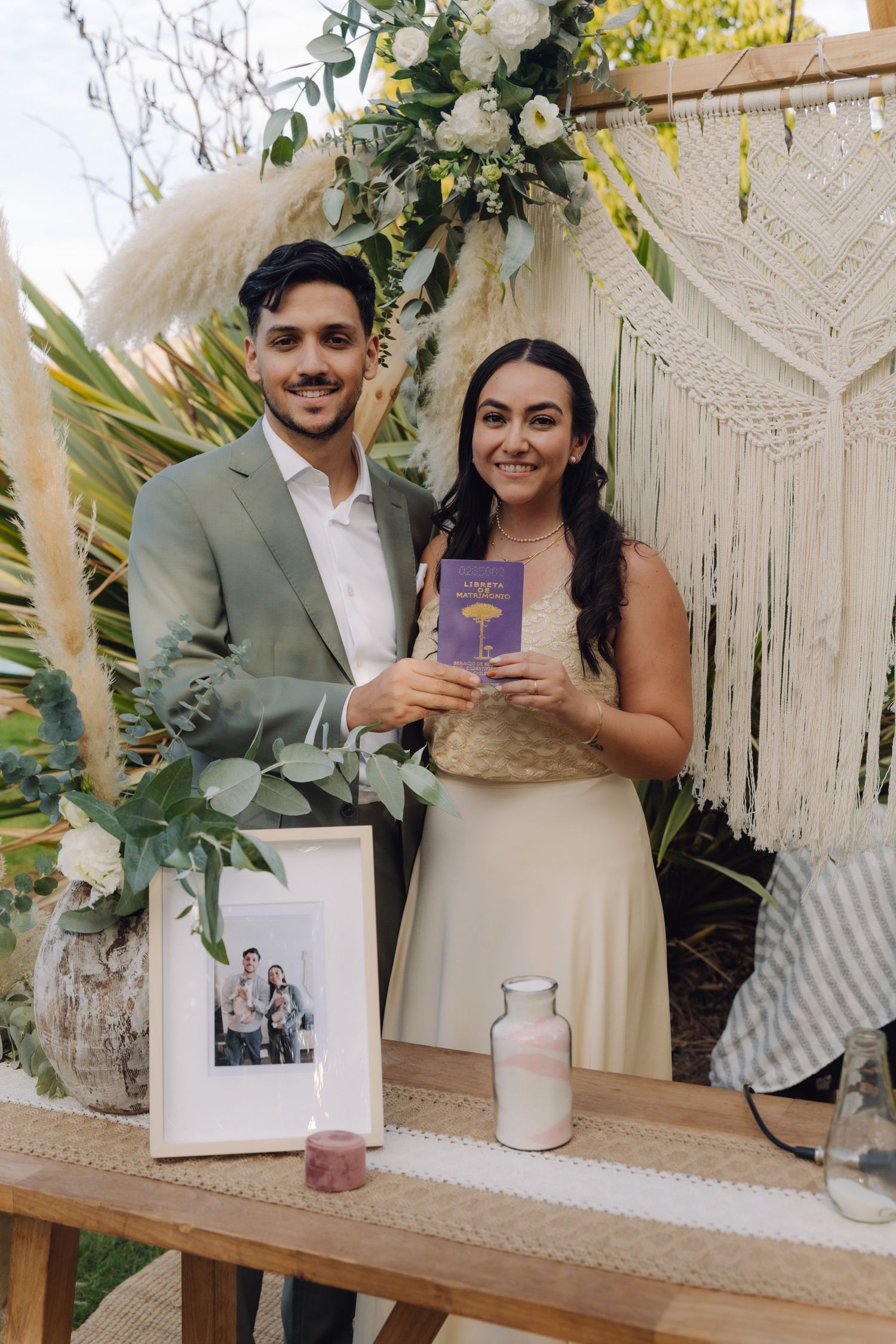 Bride and groom hold purple book at boho wedding altar with macrame backdrop.