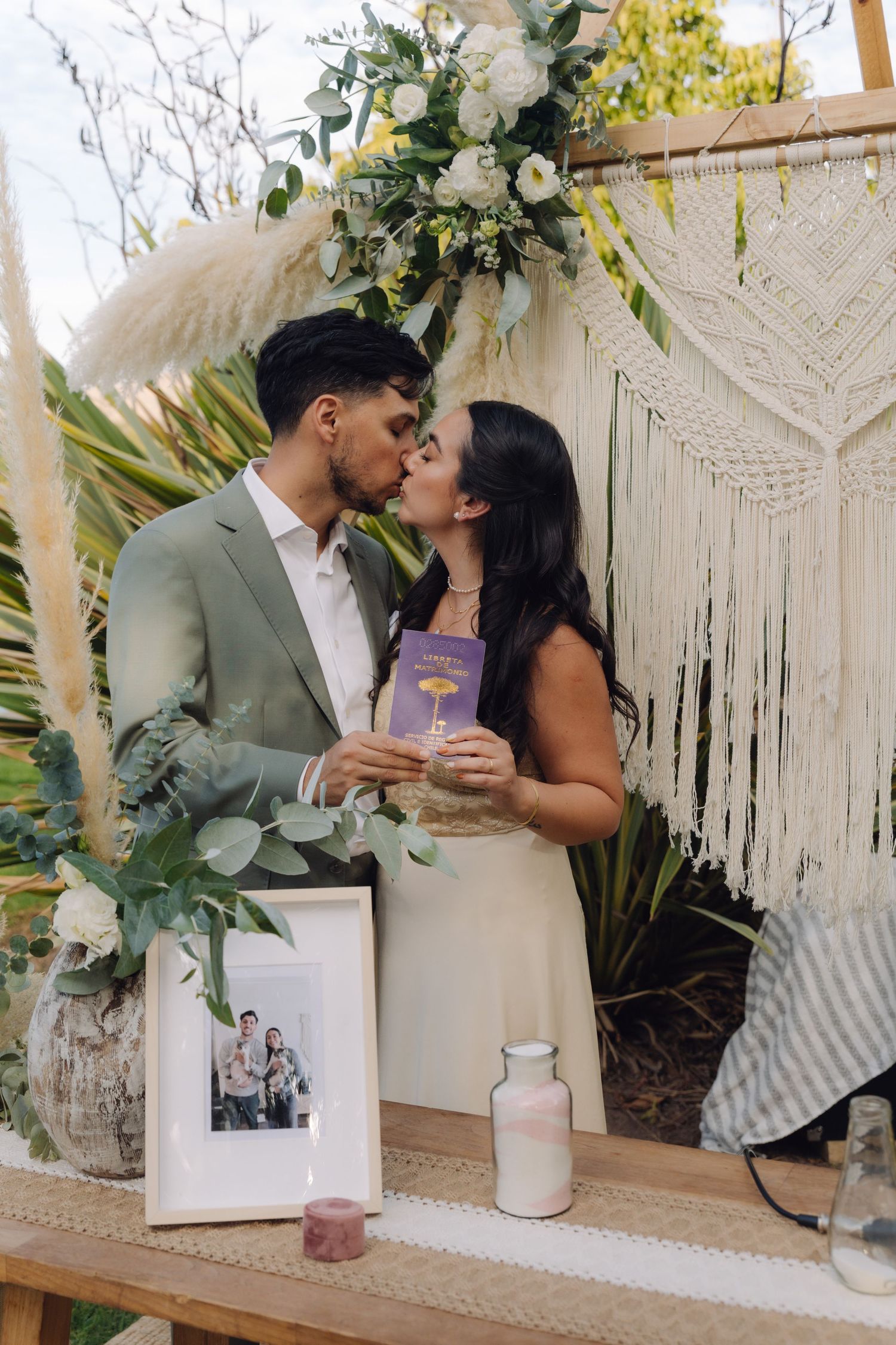 Bride and groom share a kiss at bohemian outdoor wedding ceremony altar.