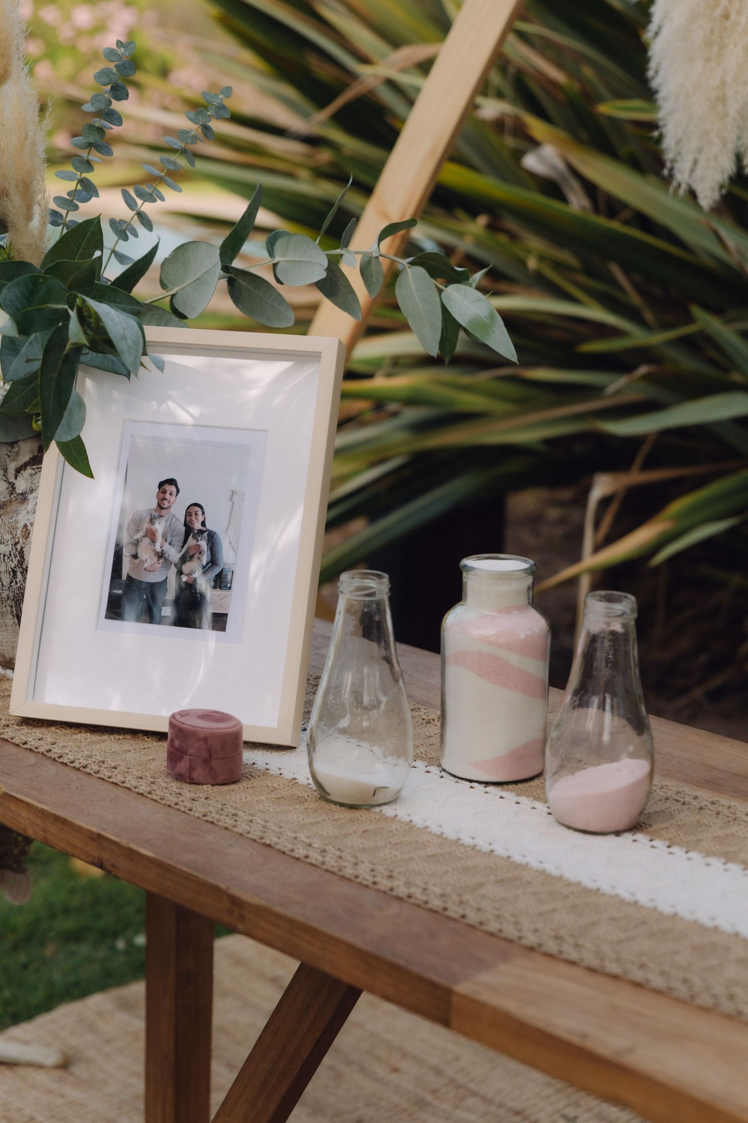 Sand ceremony vases and framed family photo displayed on rustic wooden wedding table.
