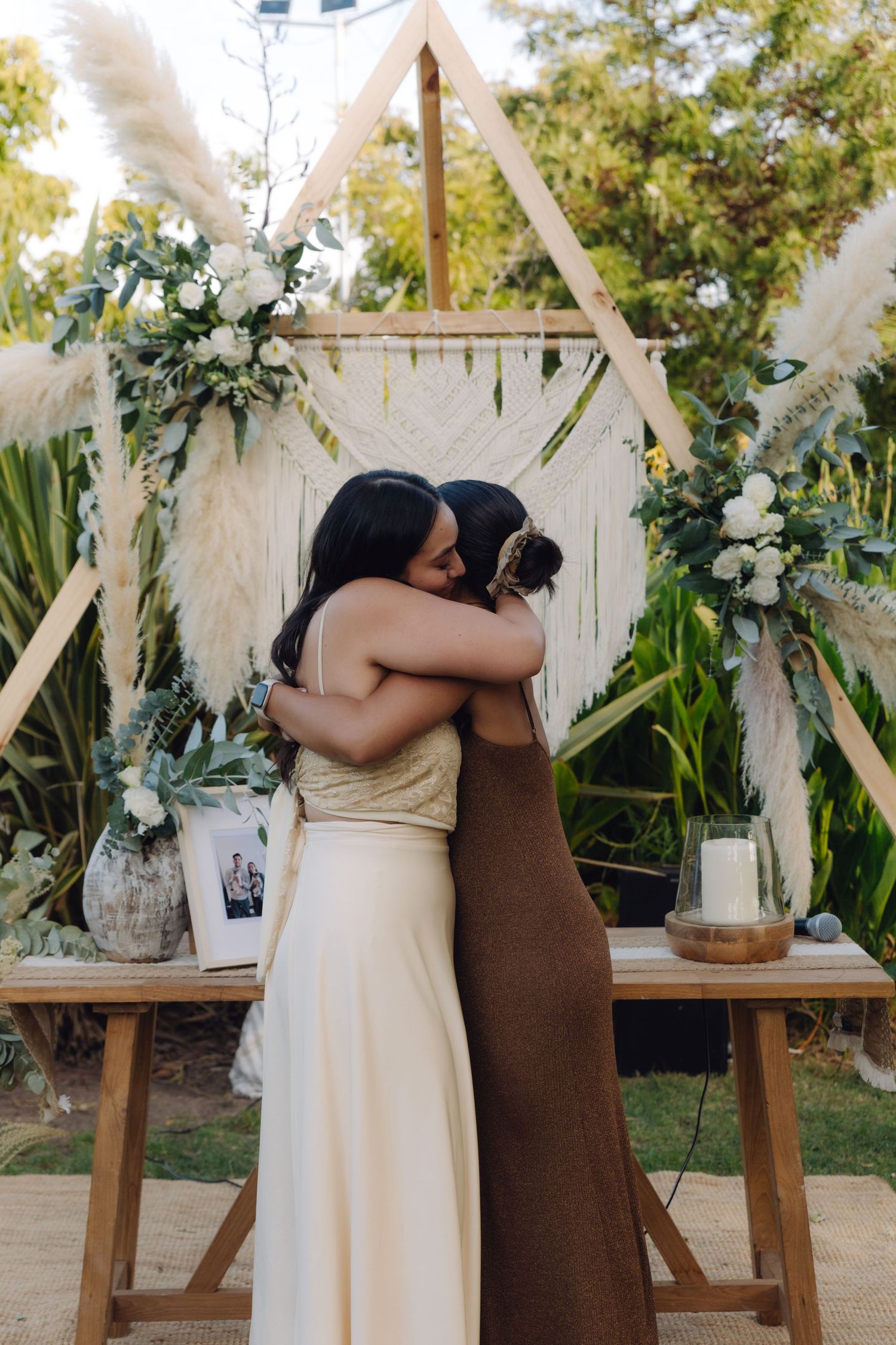 Two women share a heartfelt hug at a boho outdoor wedding ceremony altar.