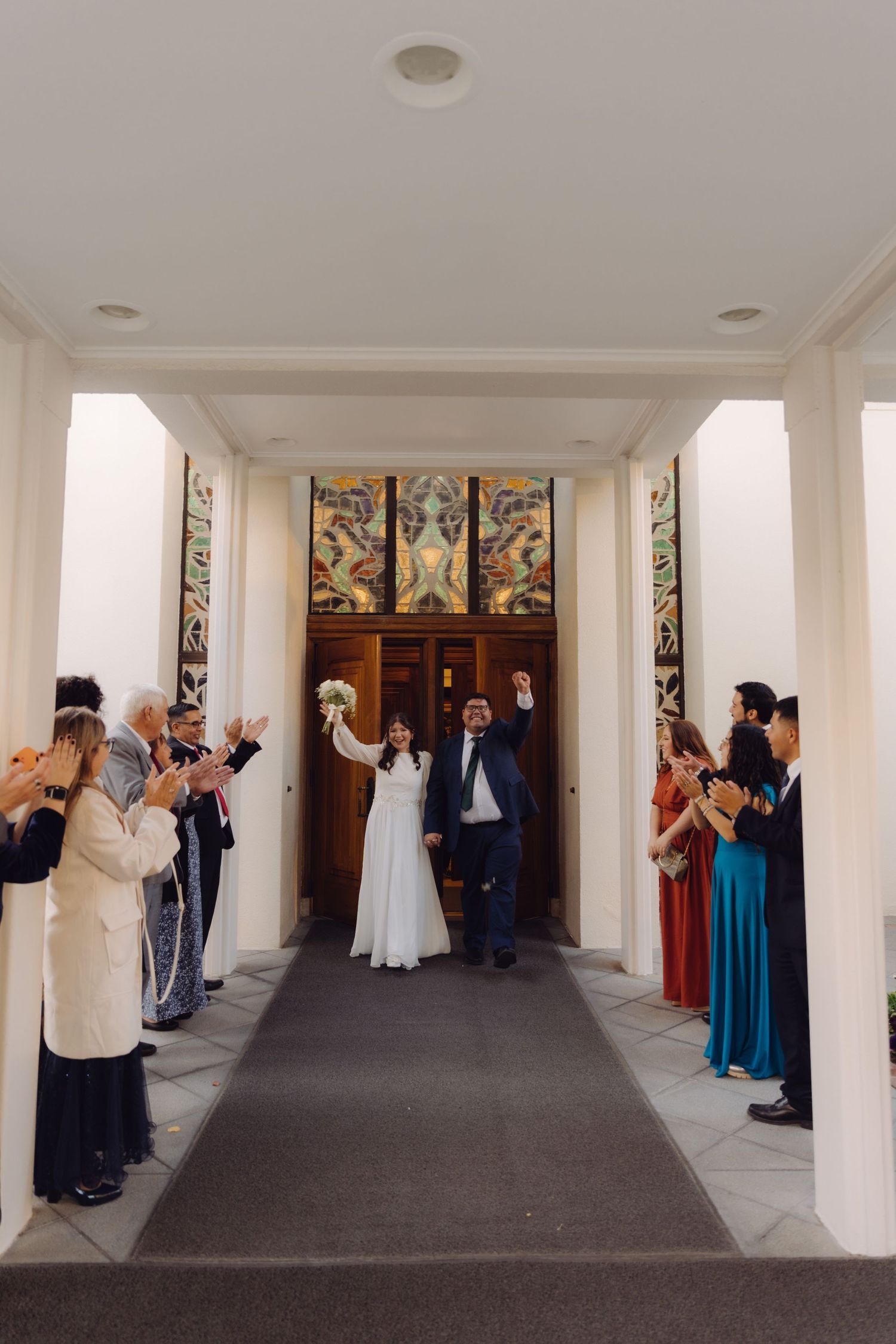 Newlyweds celebrate exit from elegant white columned building as guests applaud on both sides.