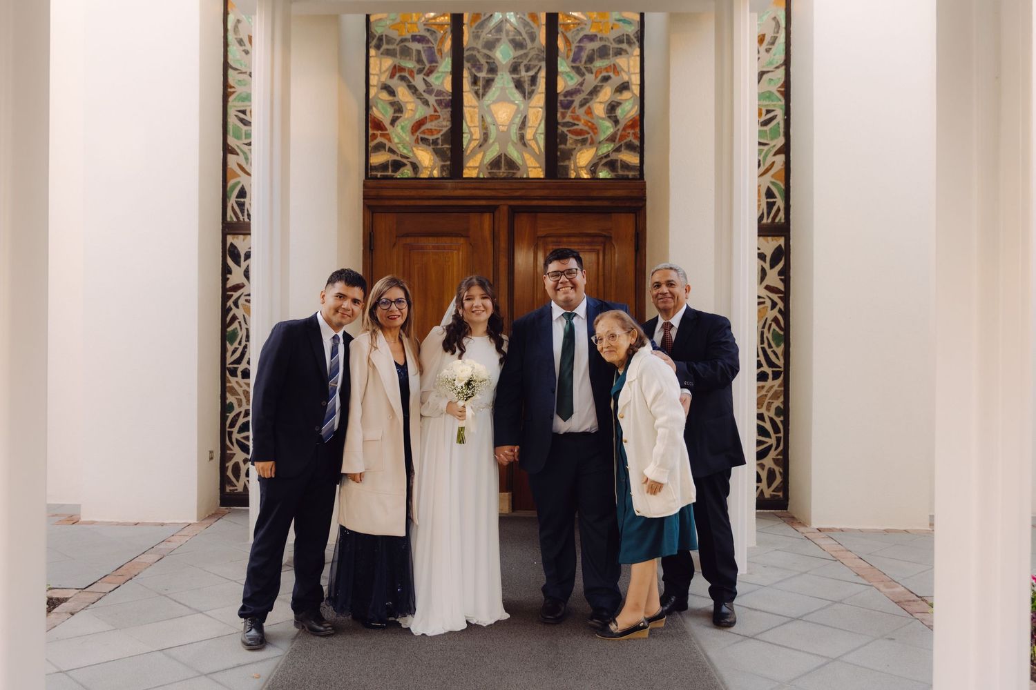 Wedding party group photo of six people posing in front of ornate wooden doors with decorative panels.