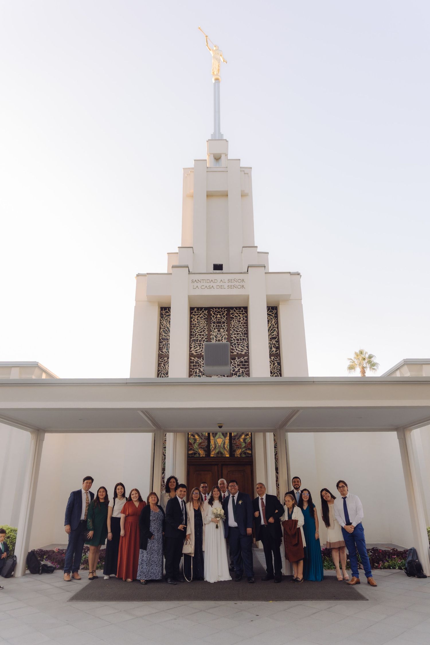 Wedding party group photo in front of a white LDS temple spire at golden hour.