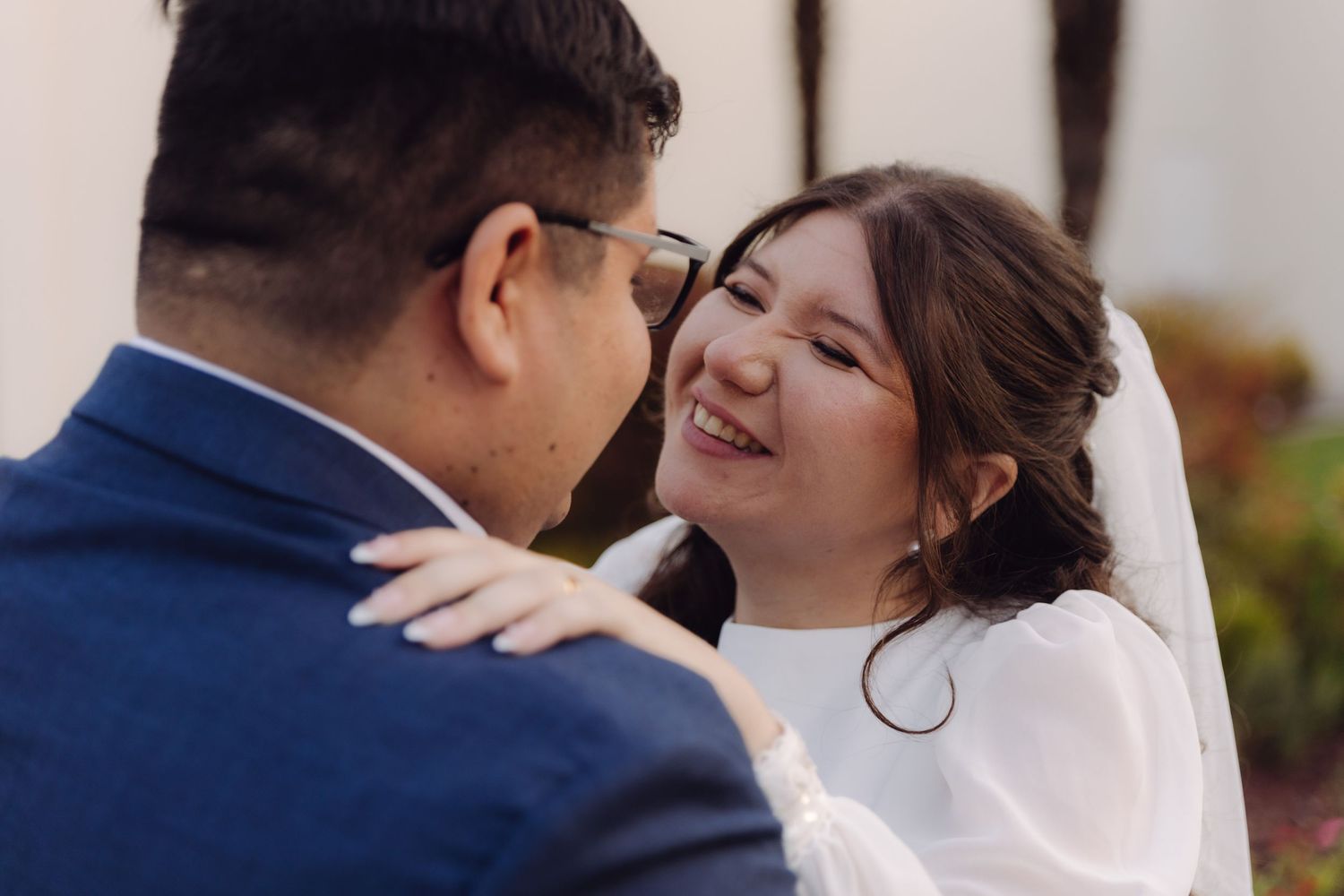Joyful bride in white wedding dress laughing with groom in navy suit during outdoor wedding photo session.