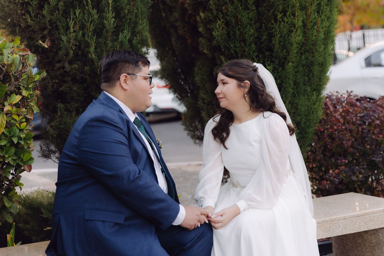 Bride and groom holding hands and gazing at each other outdoors, surrounded by autumn foliage.