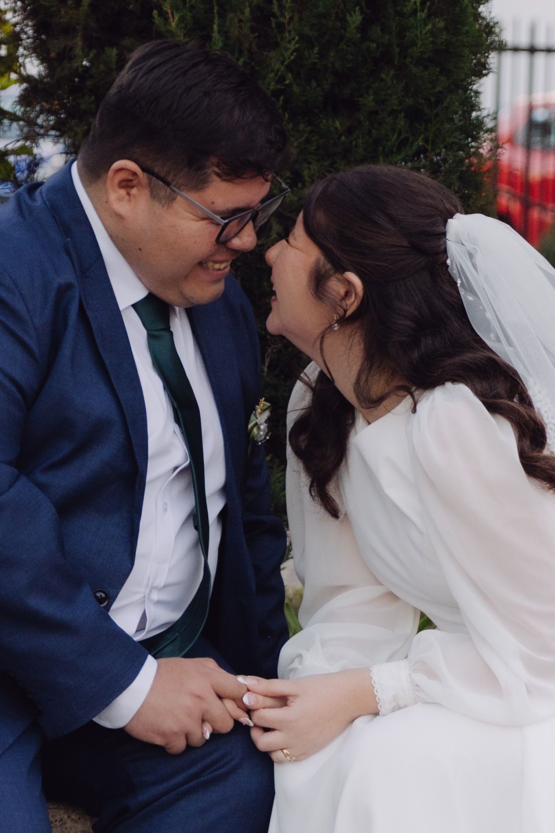 Bride and groom touch foreheads and hold hands in an intimate wedding portrait outdoors.