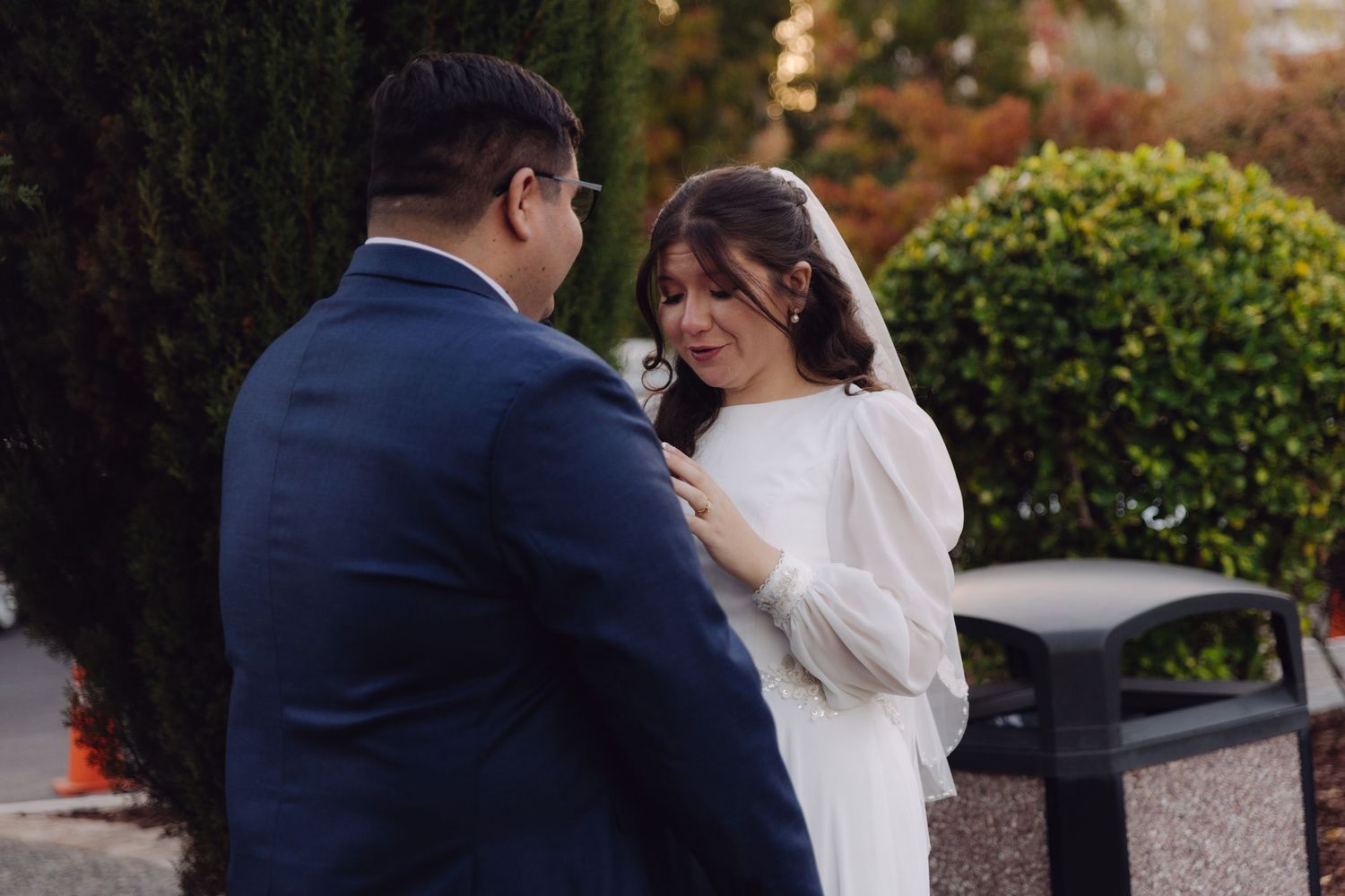 Groom pins boutonniere on bride in white wedding dress during outdoor ceremony.
