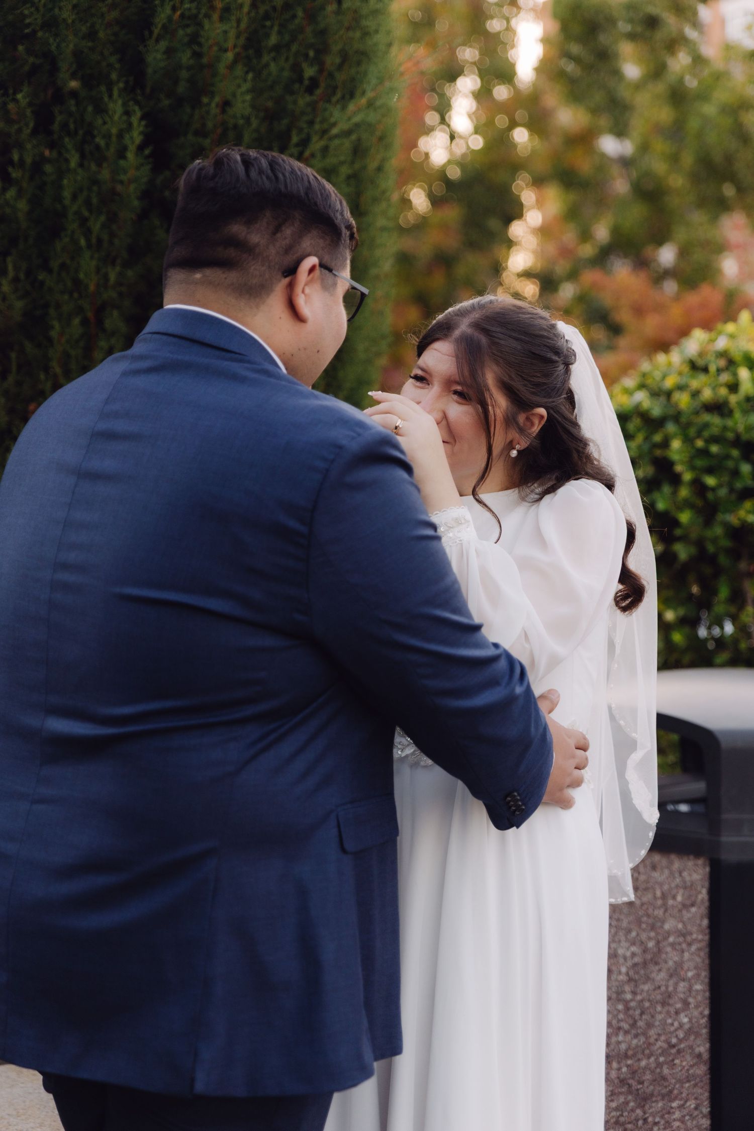 Tearful bride wipes eyes as groom comforts her during heartfelt outdoor wedding moment.