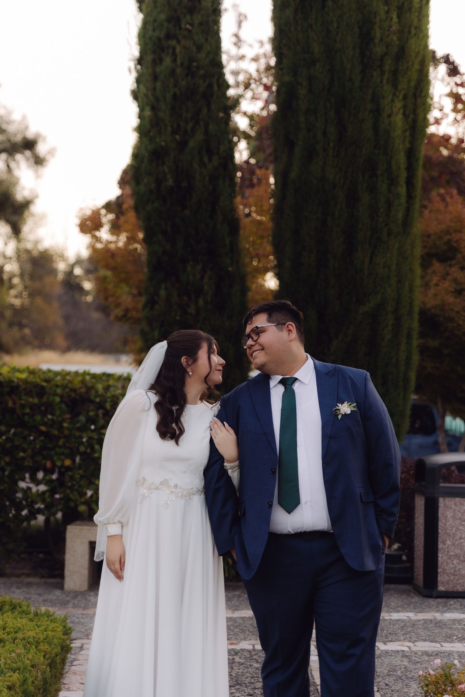Bride and groom share a joyful glance while walking in a formal garden.