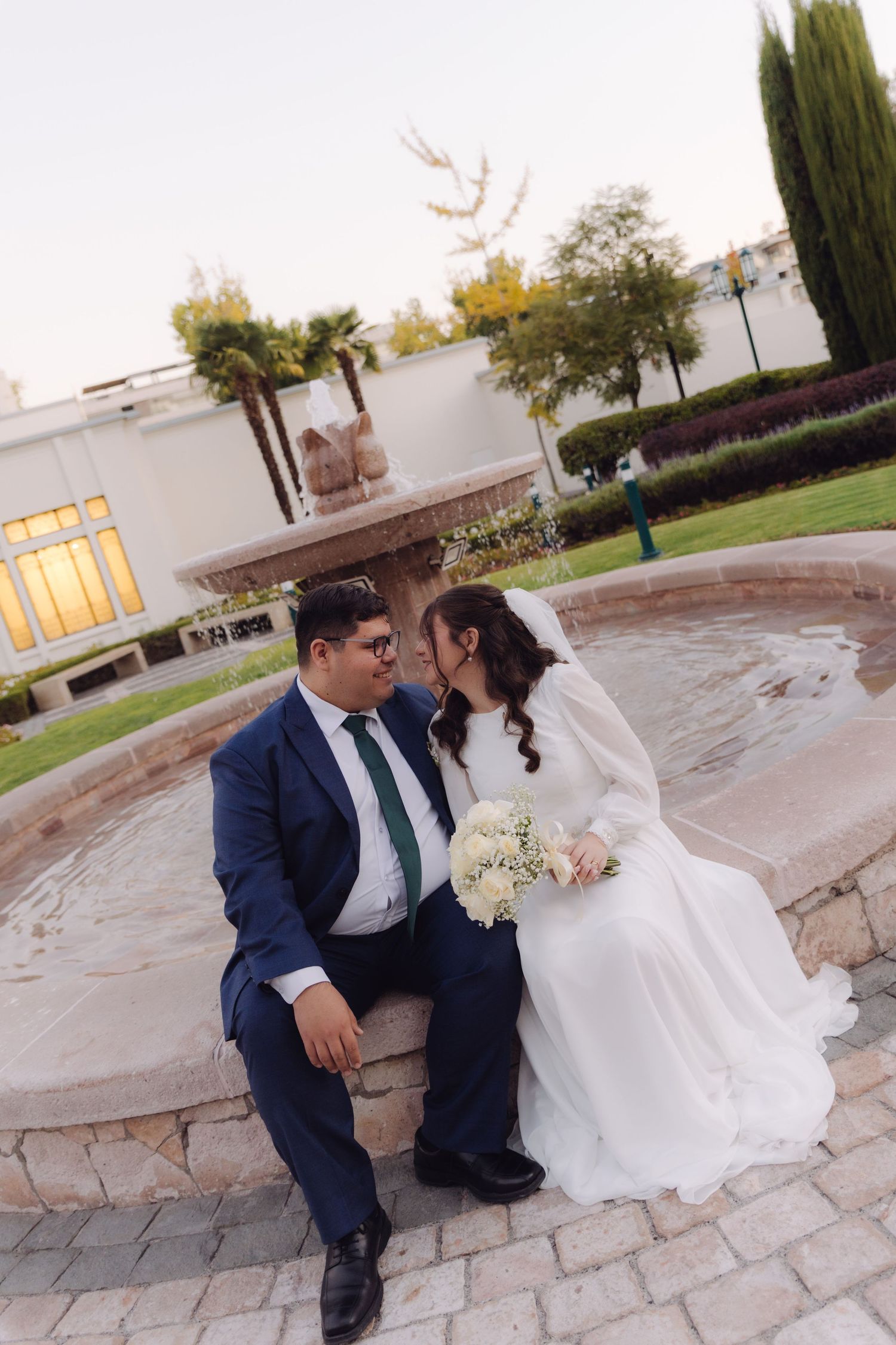 Bride and groom sitting together by a stone fountain, sharing an intimate moment at their wedding.