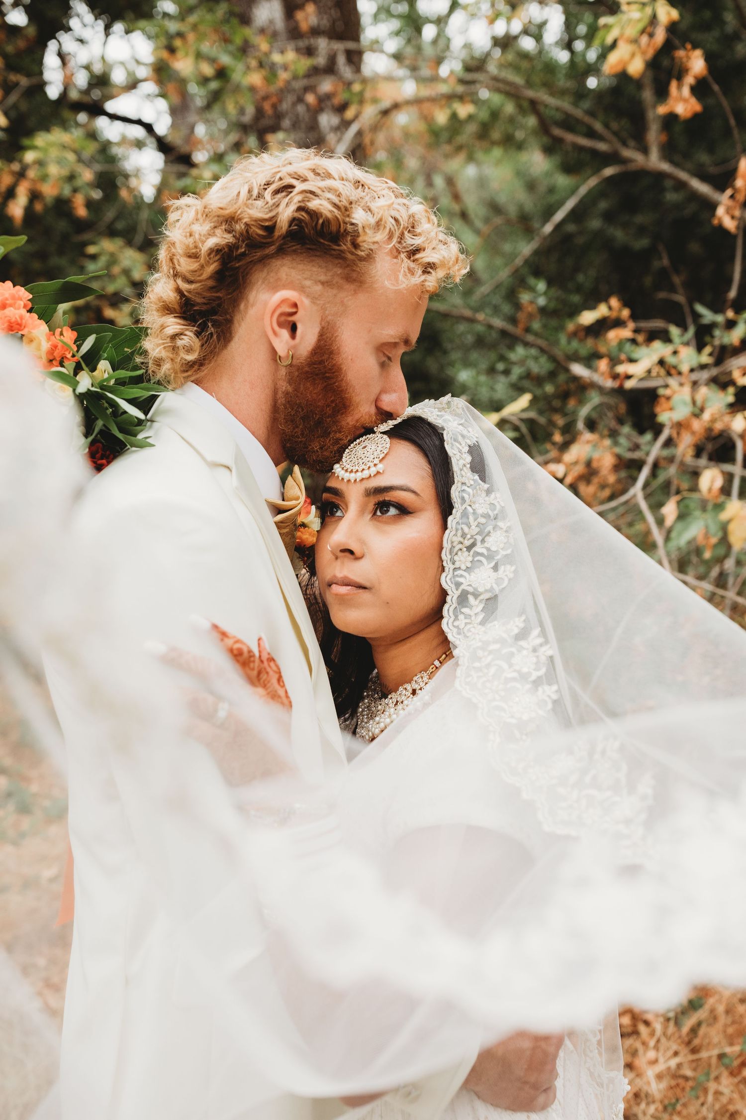 Bride and groom sharing a kiss between ornate wrought iron gates, bride holding white bouquet in elegant wedding attire.