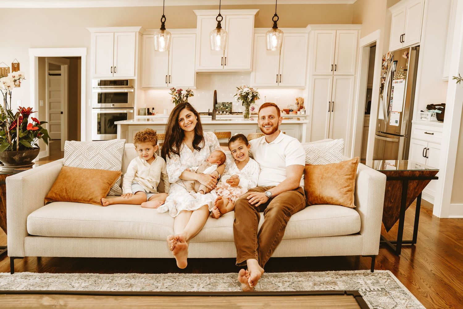 Happy family of five sitting on white sofa in bright modern home interior, lifestyle portrait.