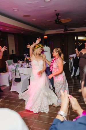 Bride in lace gown and flower crown dancing joyfully with guests at a wedding reception.