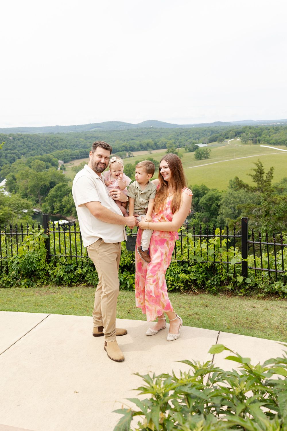 Happy family of four posing on a patio with scenic green hills and countryside views in the background.