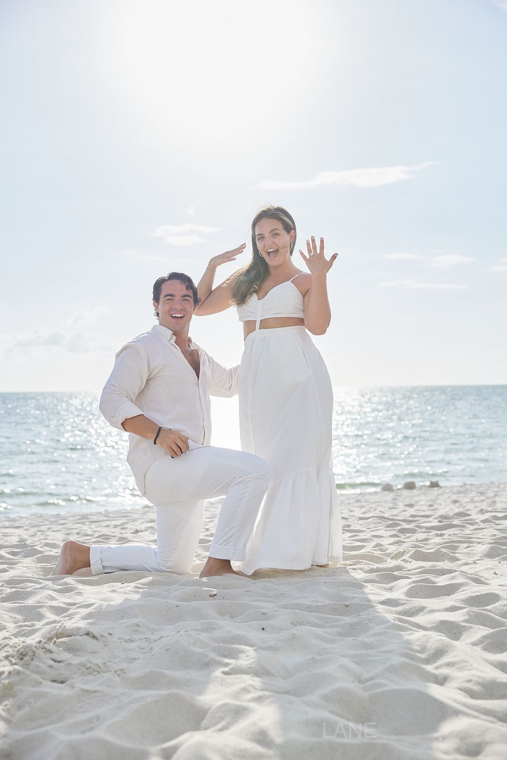 Joyful couple celebrating beach engagement with woman showing off her new ring.