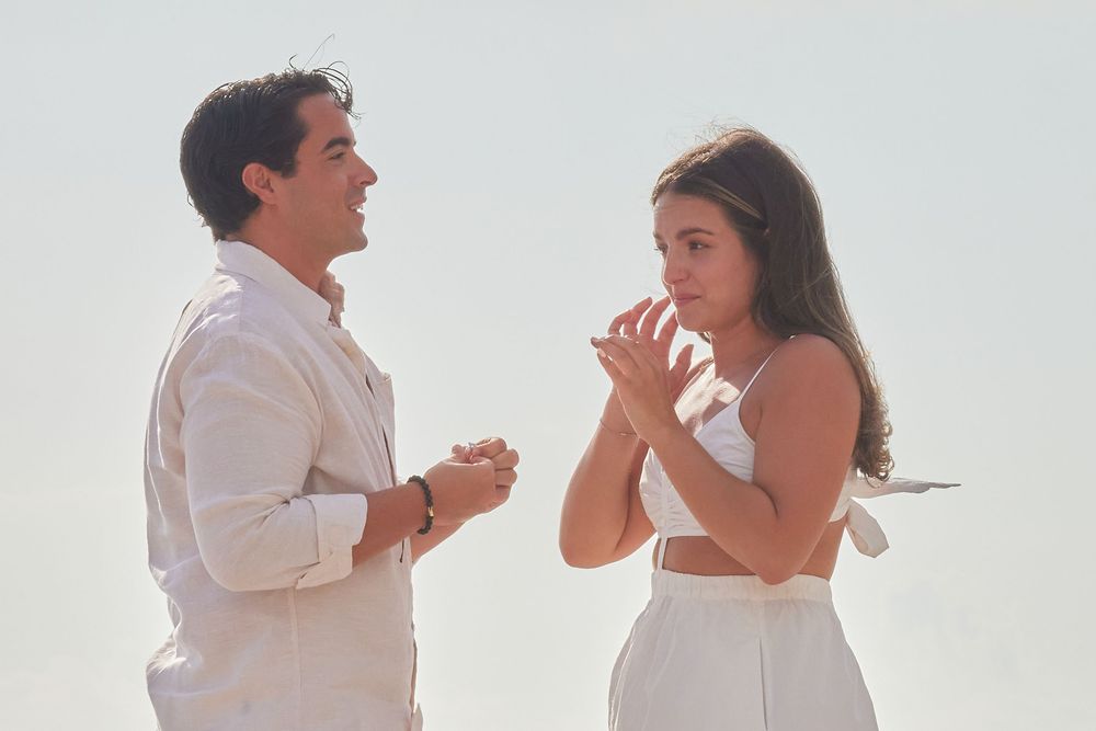 Couple in white outfits sharing a romantic moment on a bright sunny beach.