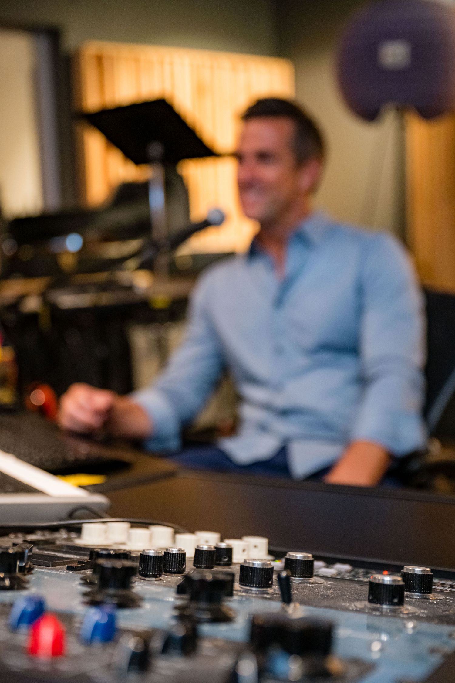 Sound engineer at mixing console in recording studio, adjusting audio equipment with knobs in foreground.
