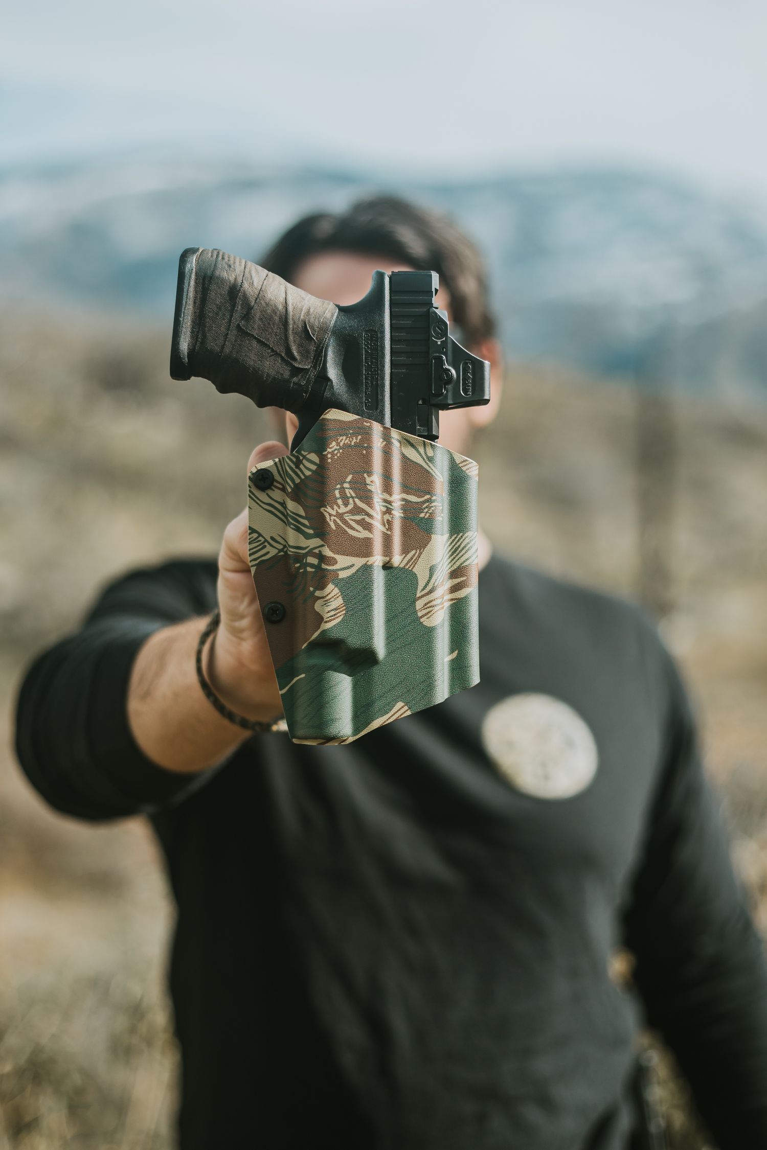 A tactical brand owner holding a Kydex holster in focus in front of his face with the Sierra Nevada mountains blurred in the background