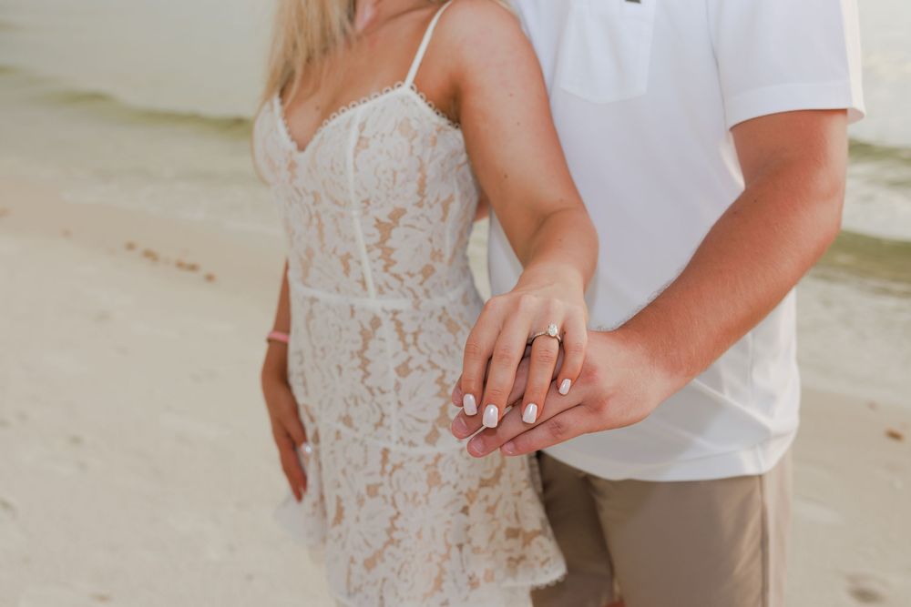 Close-up of newly engaged couple holding hands showing off diamond engagement ring on beach.