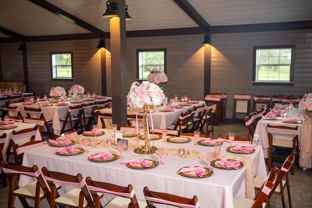 Elegant wedding reception hall with pink and white floral centerpieces, white tablecloths, and dark wood chairs.