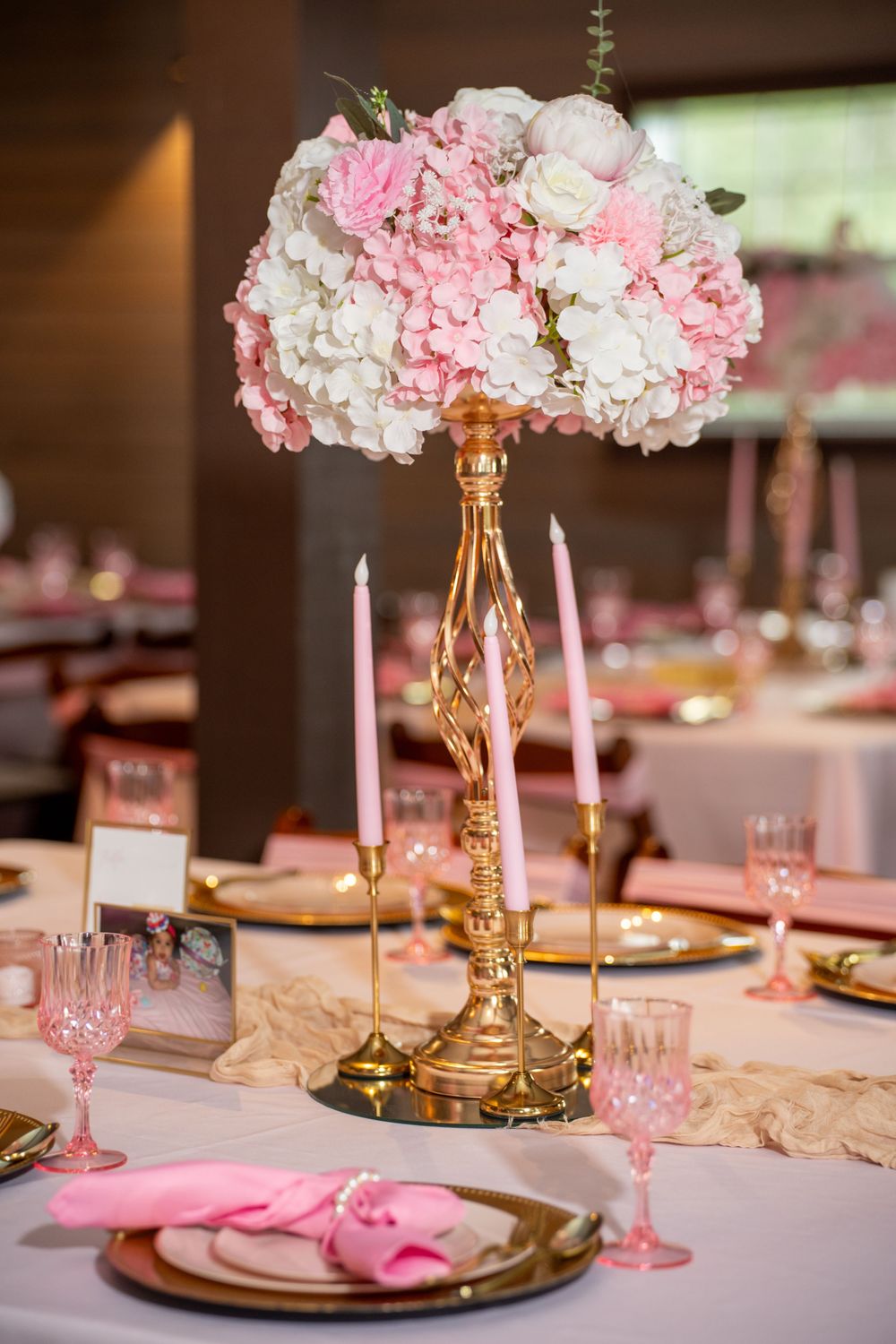 Elegant quinceanera table centerpiece with pink and white floral arrangement on gold stand with pink candles.