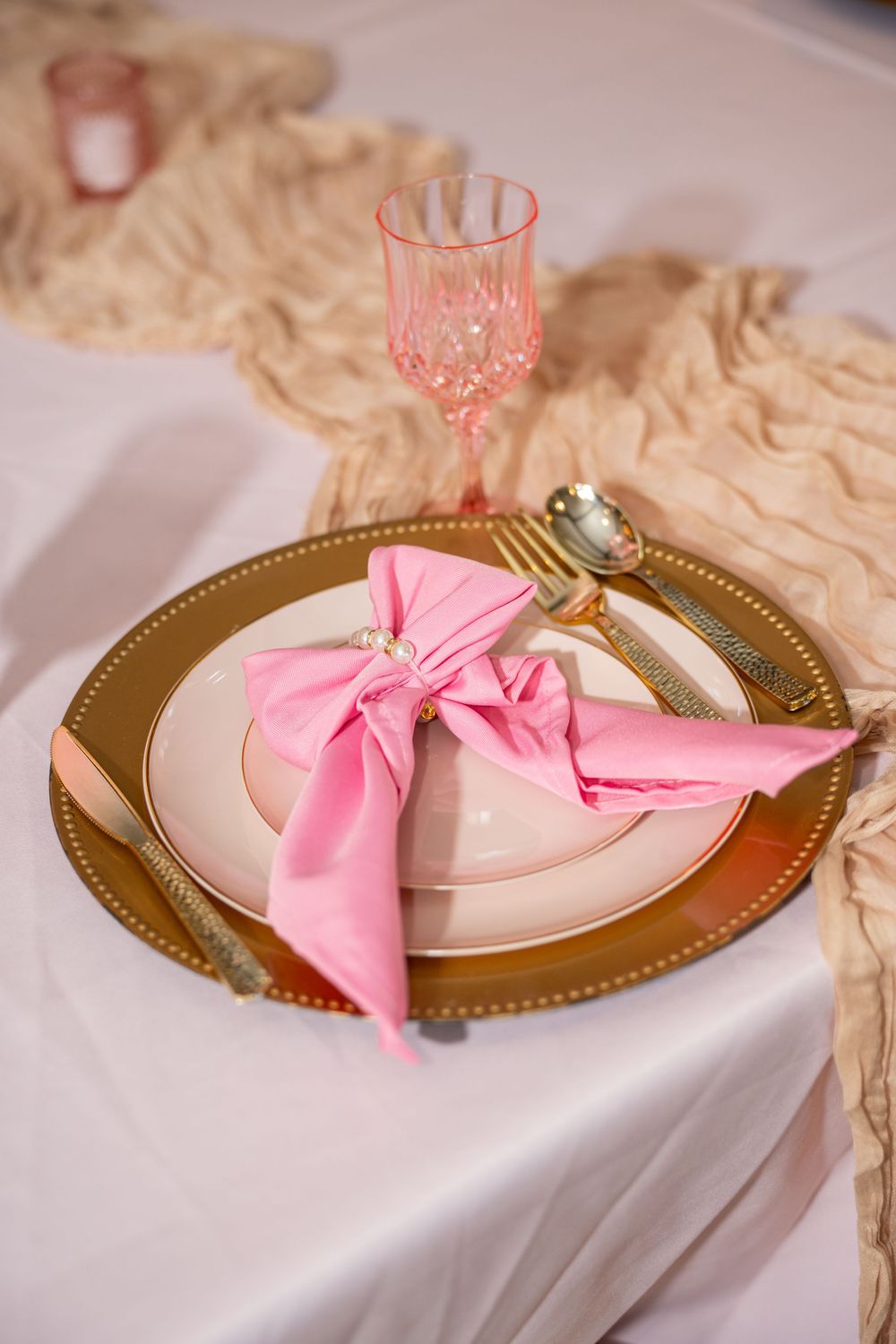 Gold charger plate with pink bow napkin and crystal glassware for quinceanera table setting.
