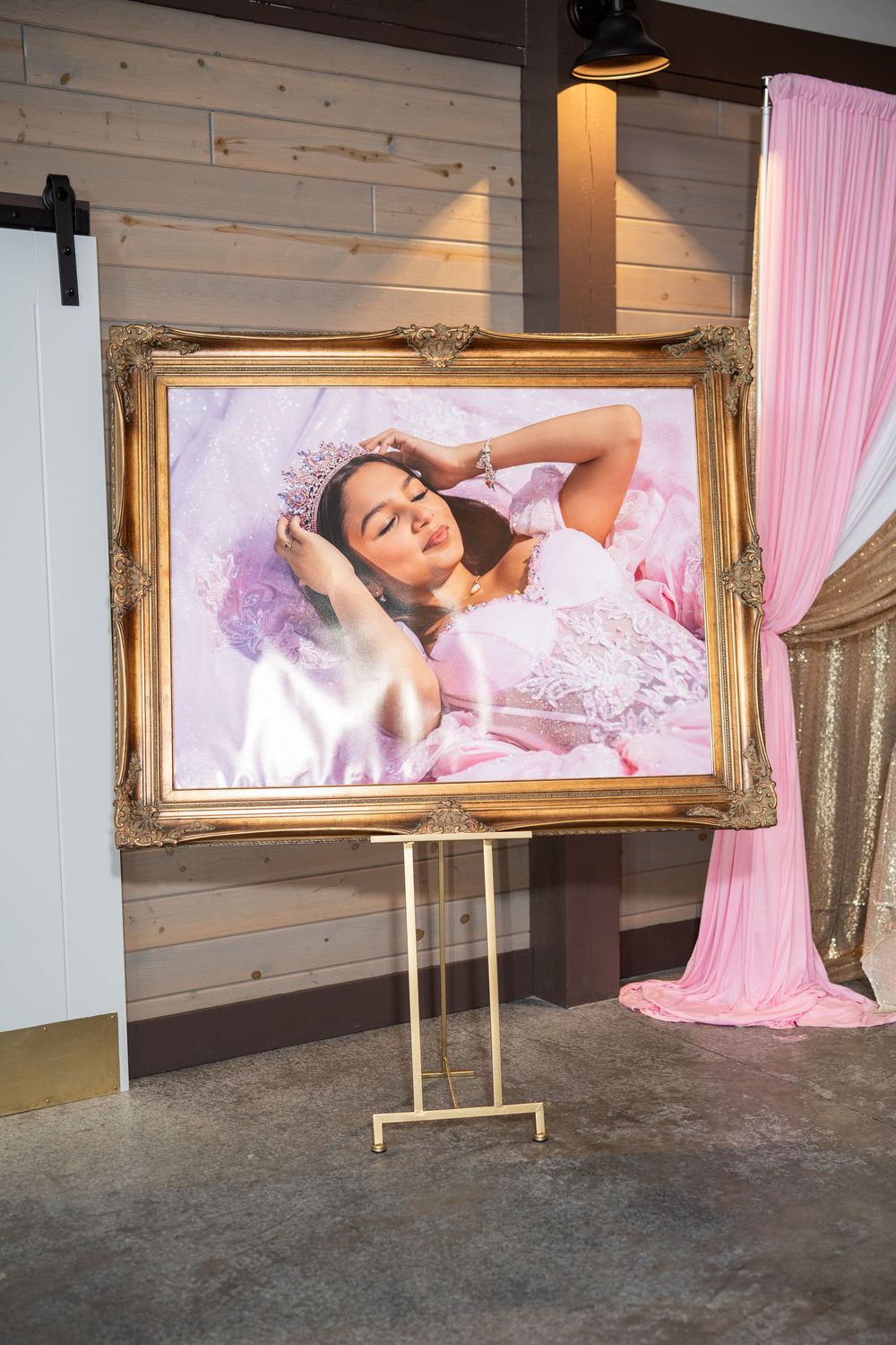 Elegant gold ornate frame on easel displaying portrait of quinceañera girl in pink gown and tiara at venue.