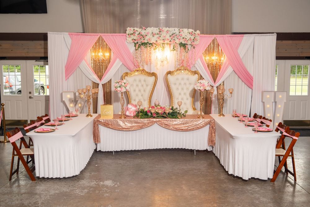 An elegant pink and gold quinceañera sweetheart table setup with floral backdrop and throne chairs.