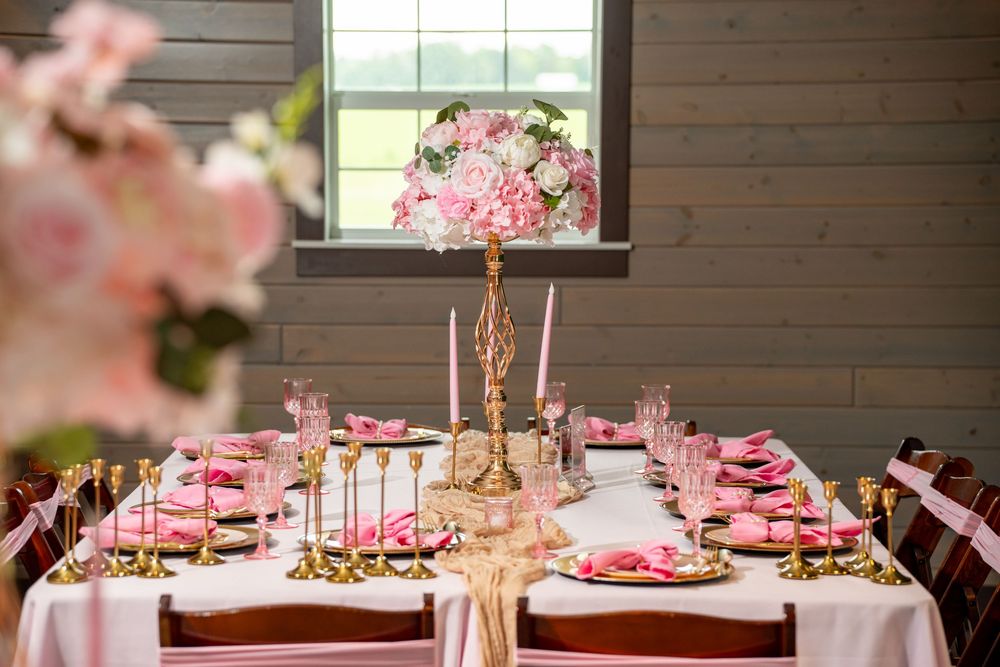 Pink and gold wedding tablescape with tall floral centerpiece, taper candles, and elegant place settings.