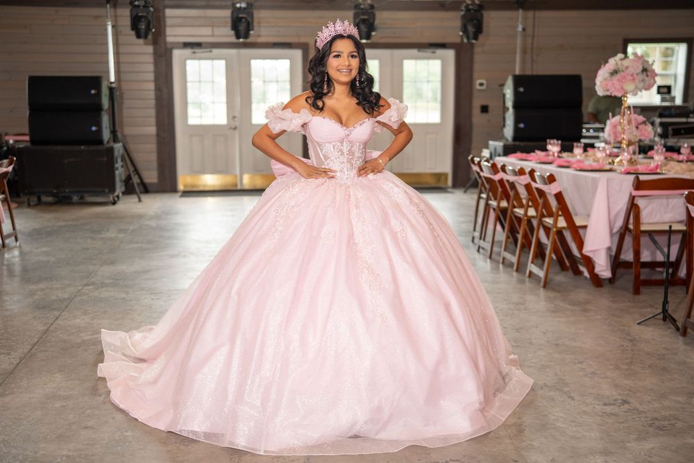 Young woman in a pink ball gown and tiara poses gracefully at her quinceanera celebration in a decorated venue.