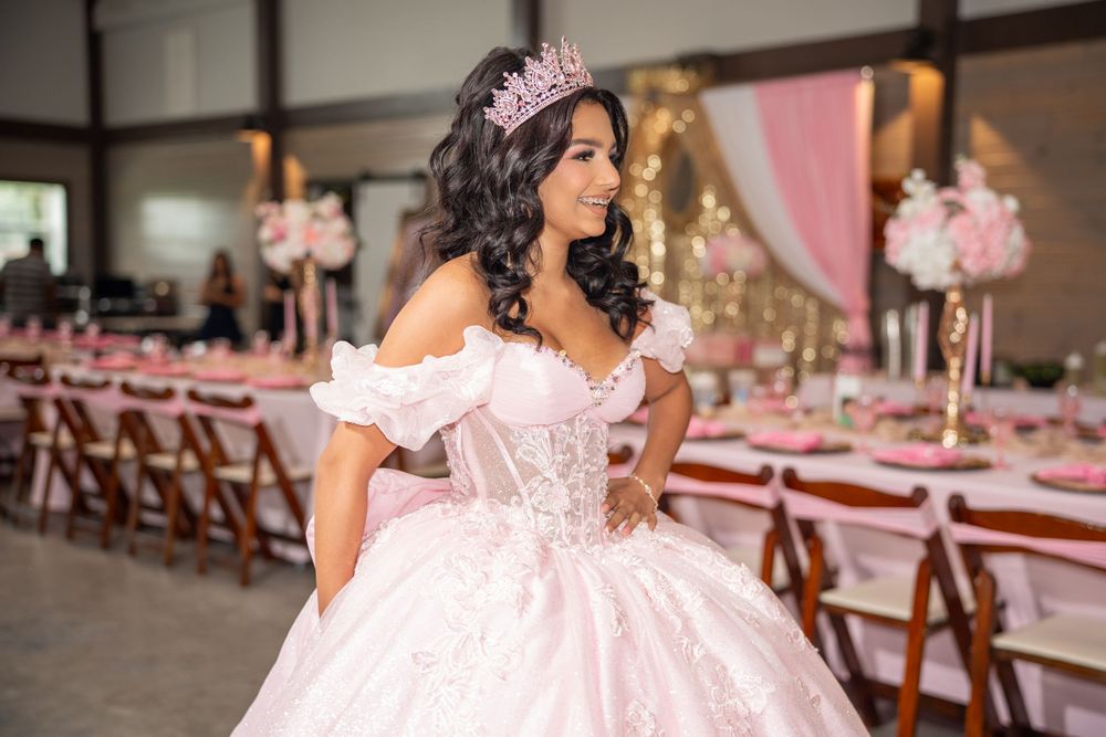 Young woman in pink ball gown and tiara posing at her elegant pink quinceanera celebration.