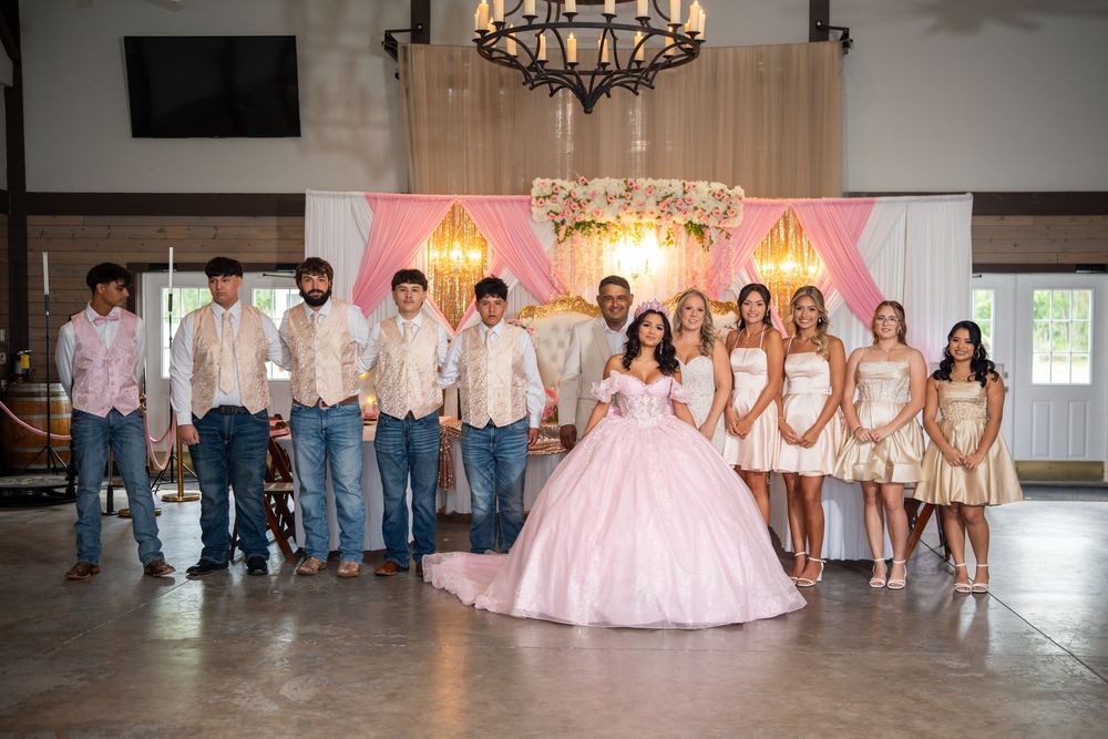 Quinceanera court group photo with girl in pink ball gown surrounded by chambelanes and damas.