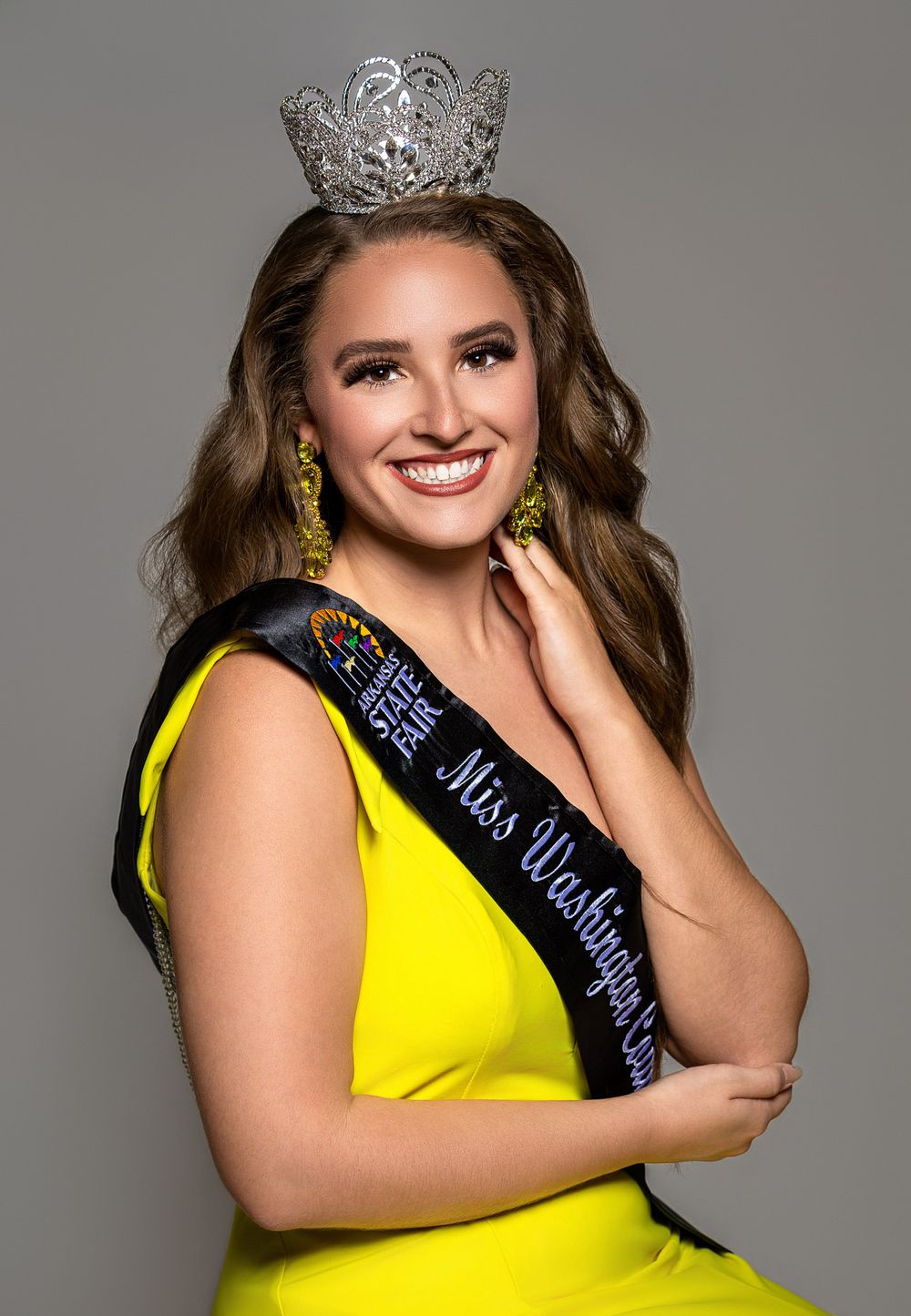 Woman in yellow dress wearing Miss Washington crown and sash, smiling confidently in a pageant portrait photo.