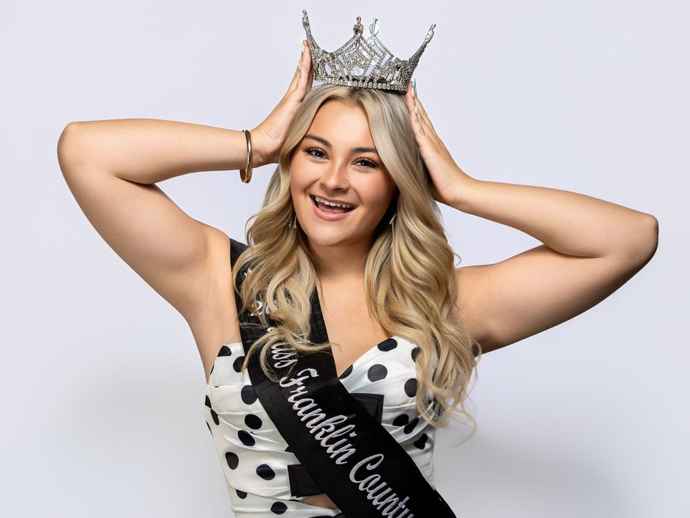 Young woman wearing a Franklin County queen crown and sash, smiling confidently in a polka dot top.