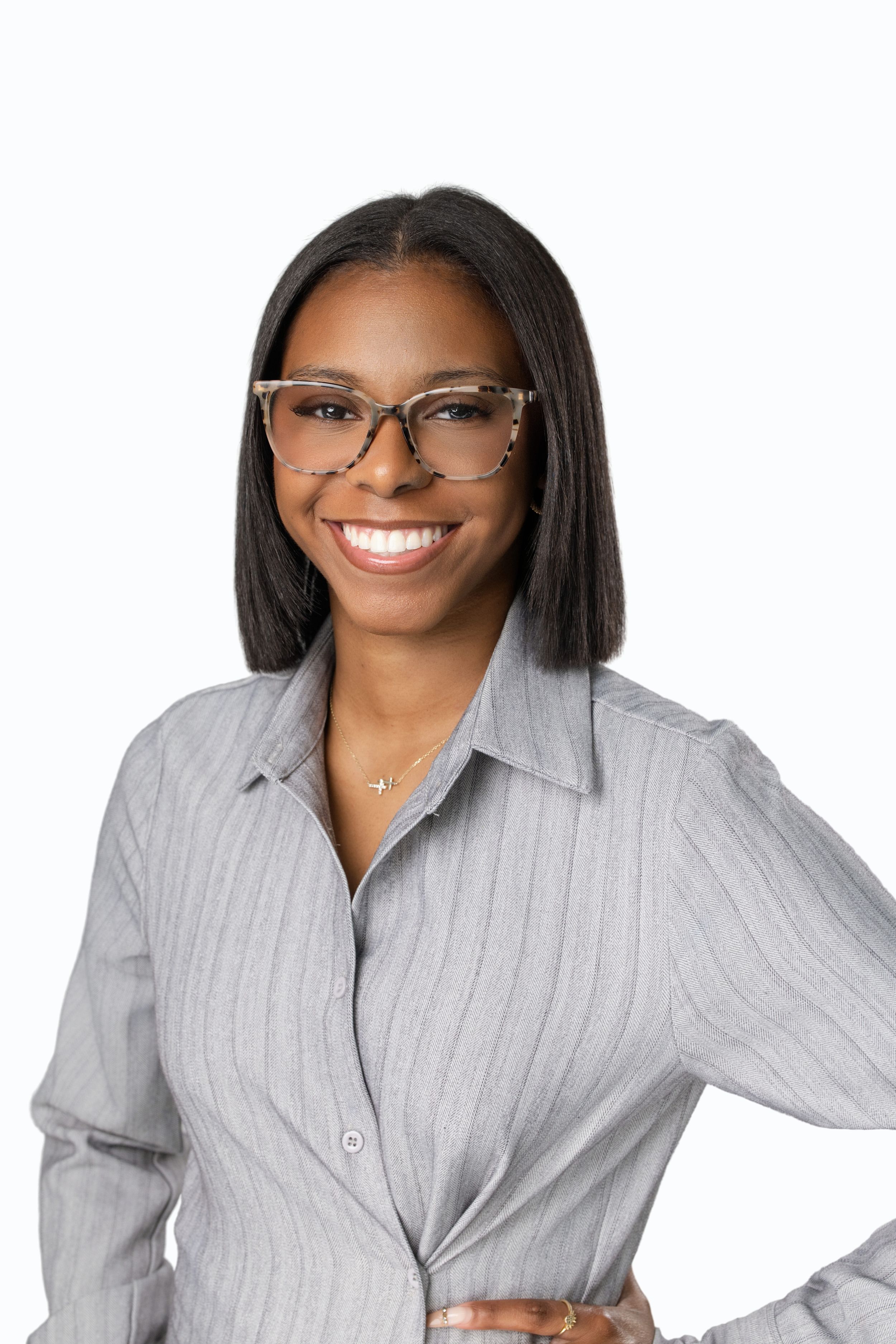Smiling professional woman wearing glasses and gray striped blouse posing confidently against white background.
