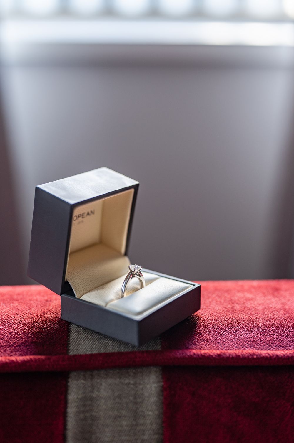 Diamond solitaire engagement ring displayed in an open gray jewelry box on a red velvet surface.